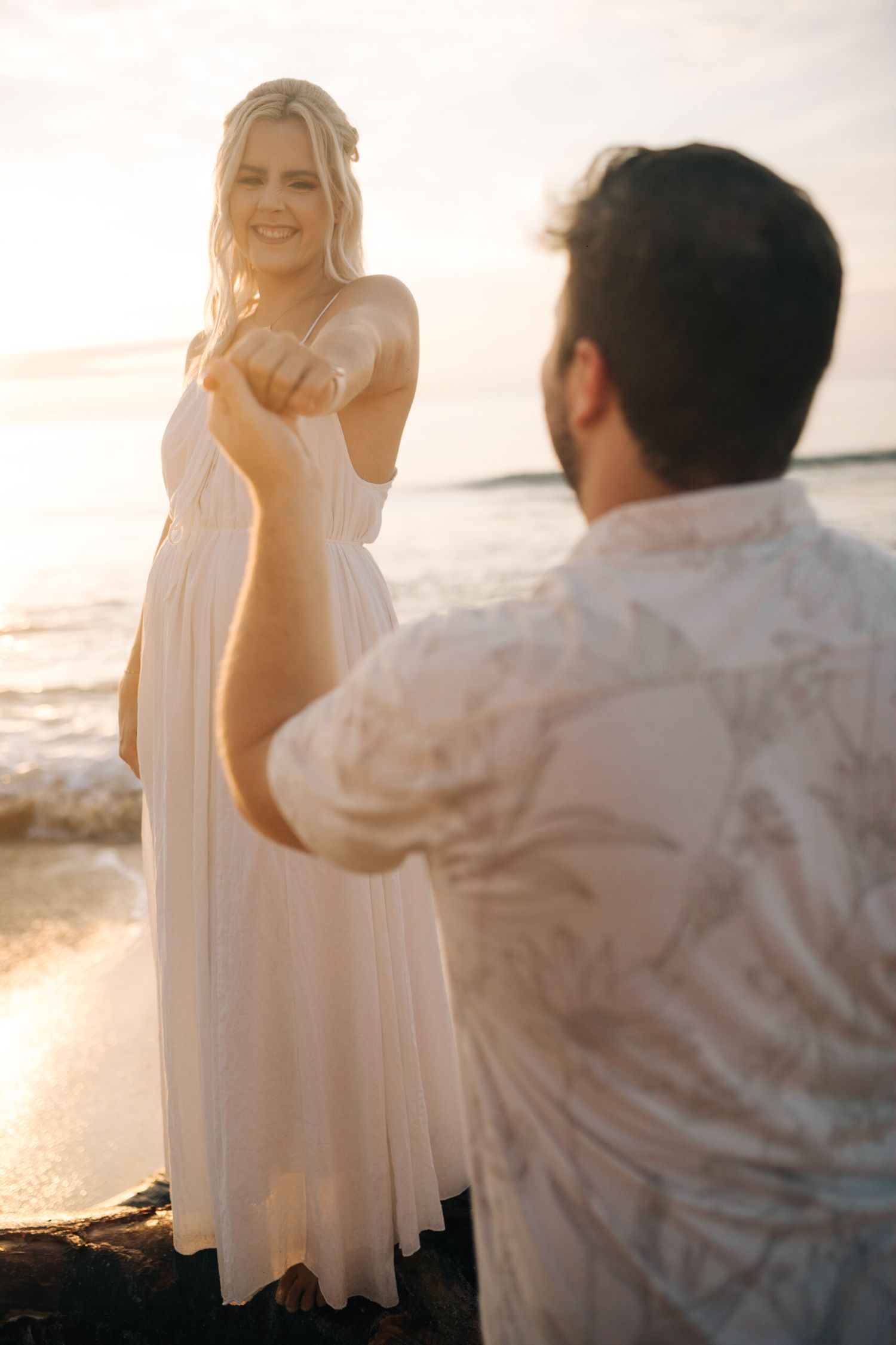 A sunset beach proposal moment captured with ocean waves in the background.