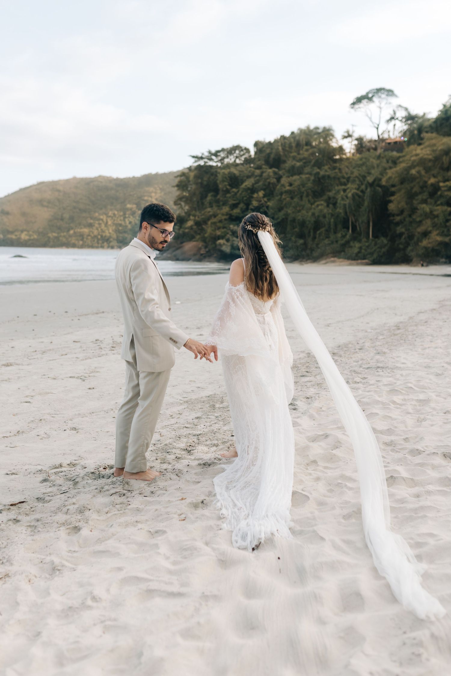 Seaside wedding portrait with couple standing on sandy beach near coastal cliffs.
