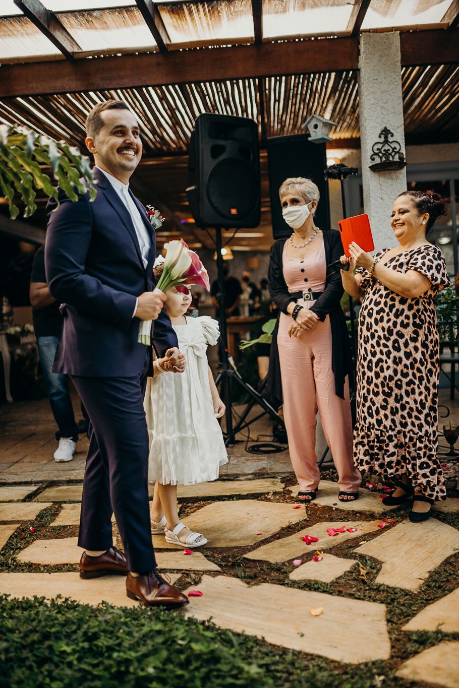 Wedding guests gather on stone pavers under a rustic covered patio during celebratory moments.