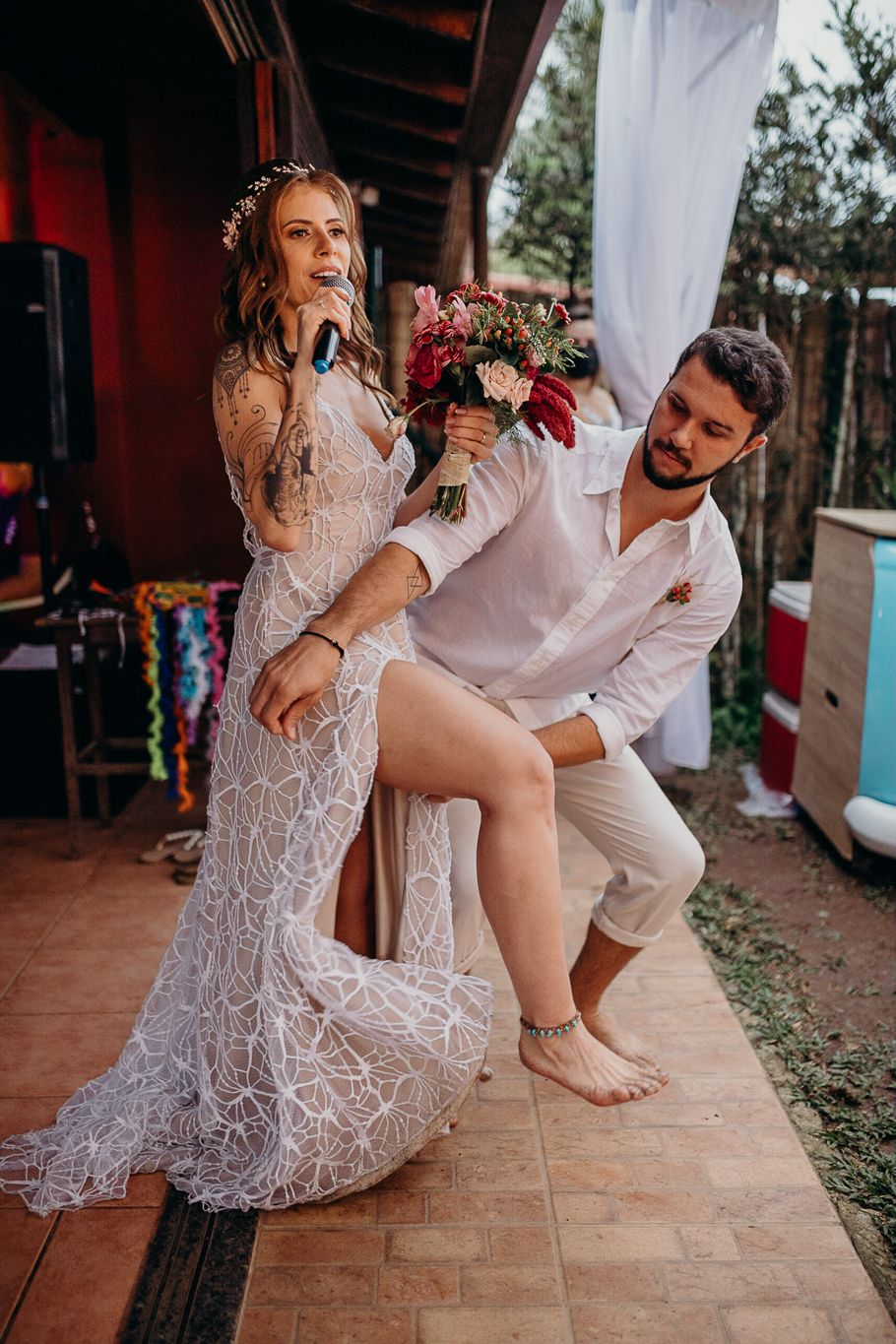 A couple shares playful moments in white wedding attire on a tiled outdoor patio.
