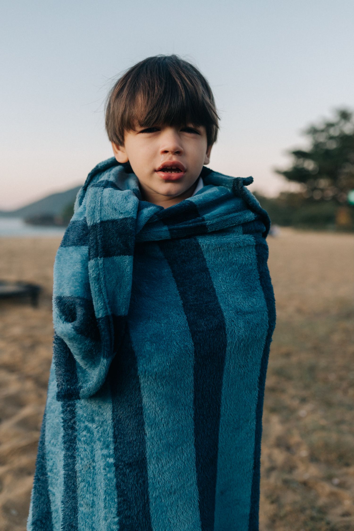 Child wrapped in blue striped blanket standing outdoors at dusk.