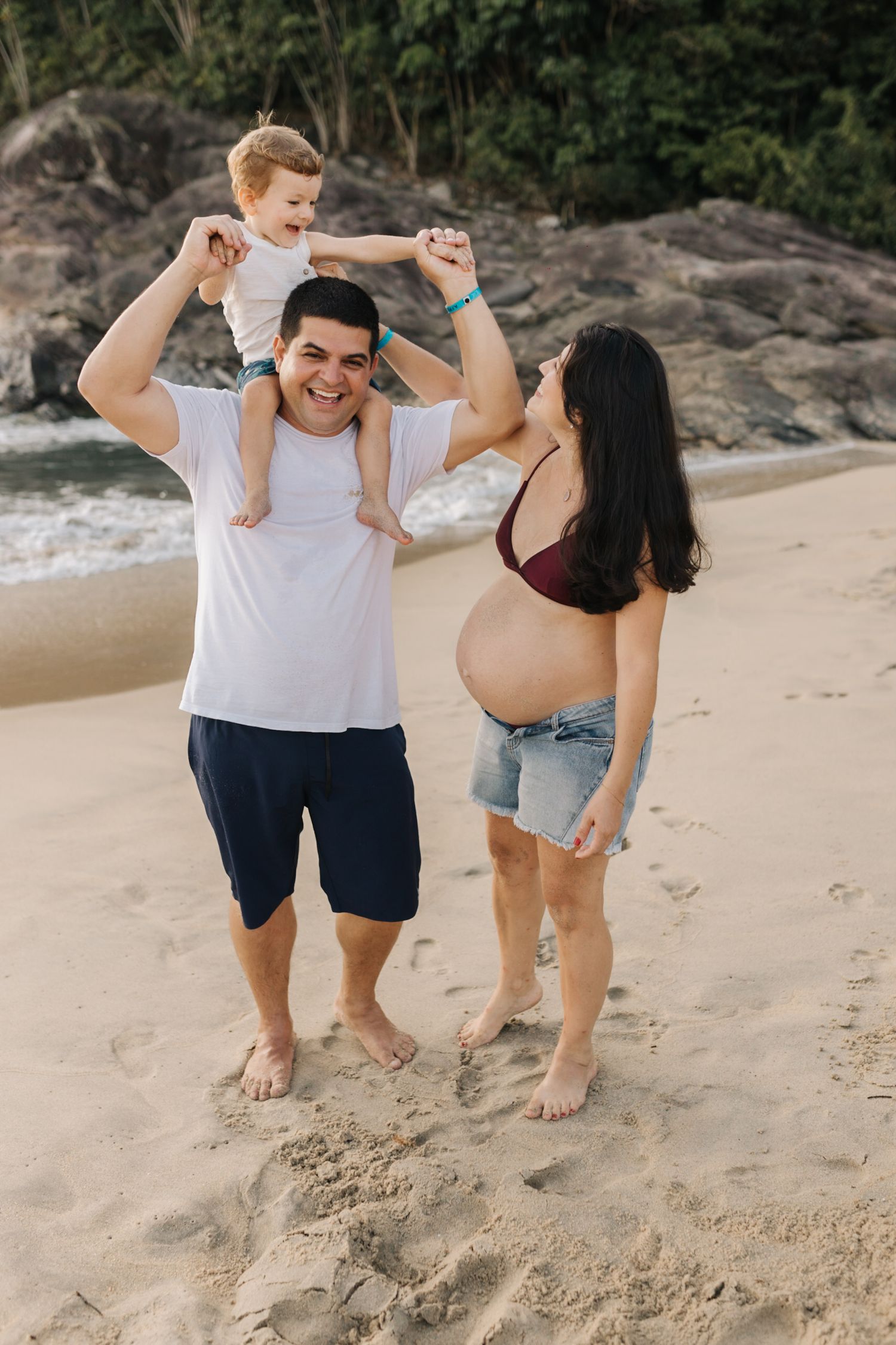 Family members interacting playfully on beach sand with natural coastal background.