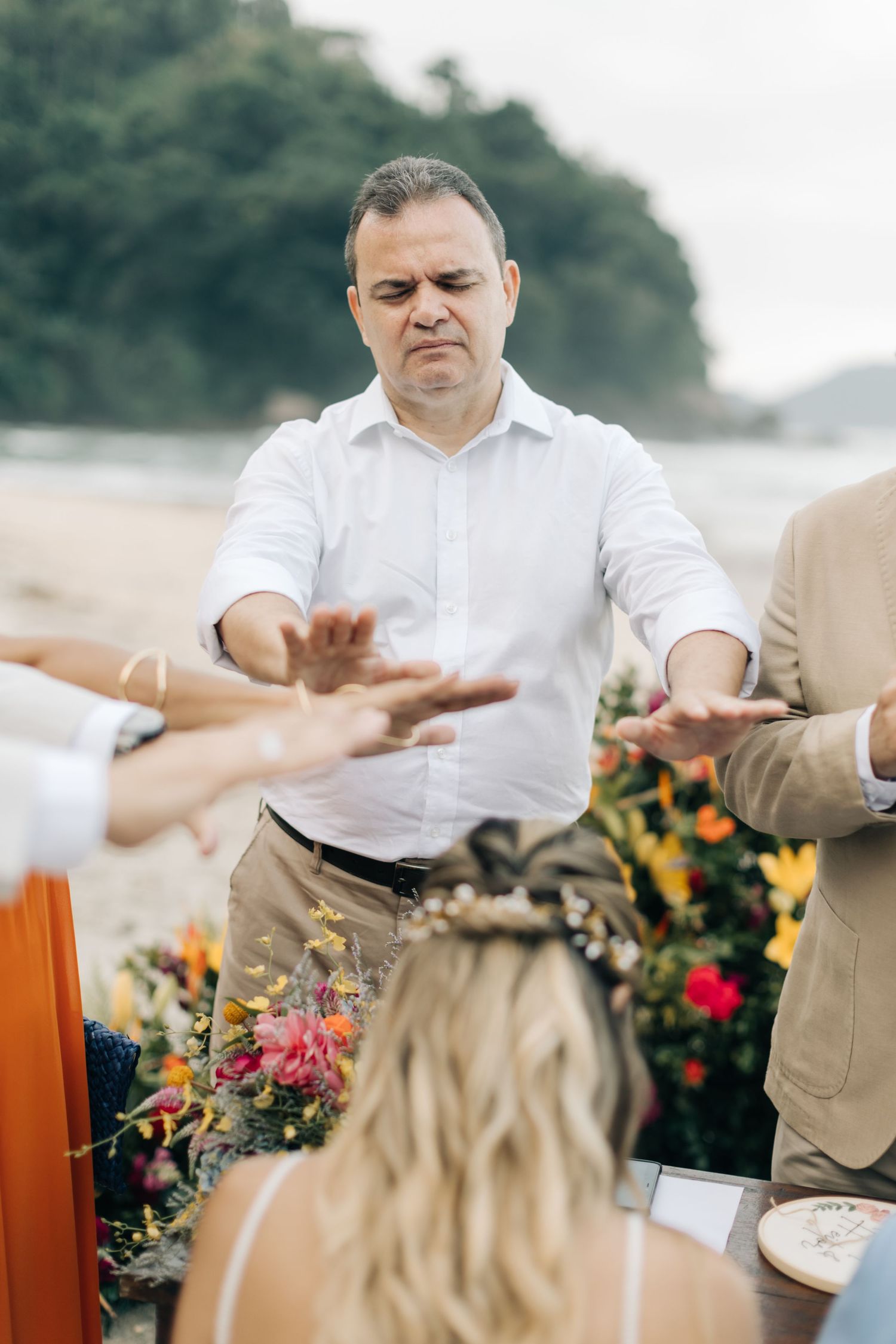 Wedding officiant gesturing during beach ceremony with colorful floral arrangements.