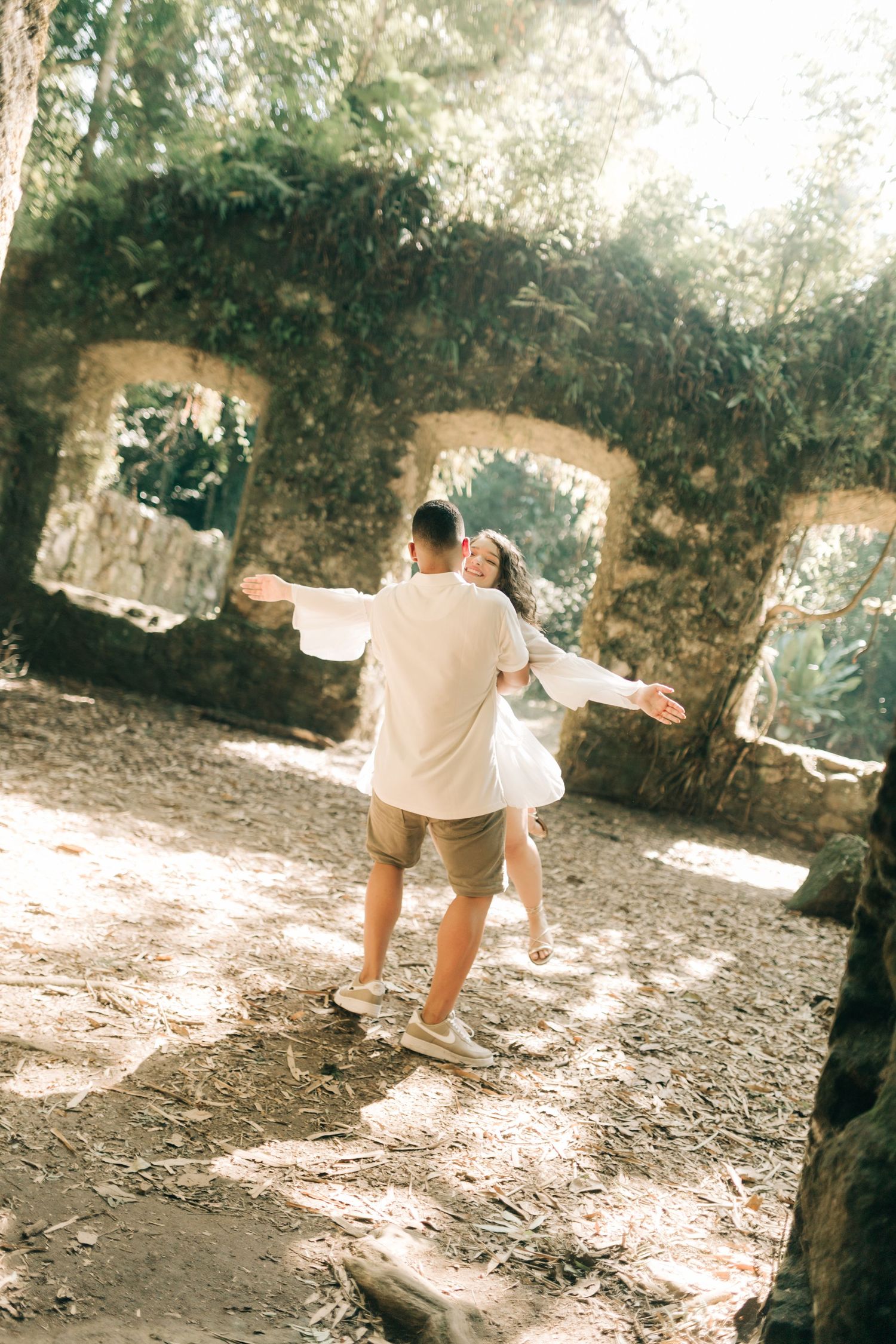 Dancing couple captured in sunlit stone ruins during romantic photoshoot.