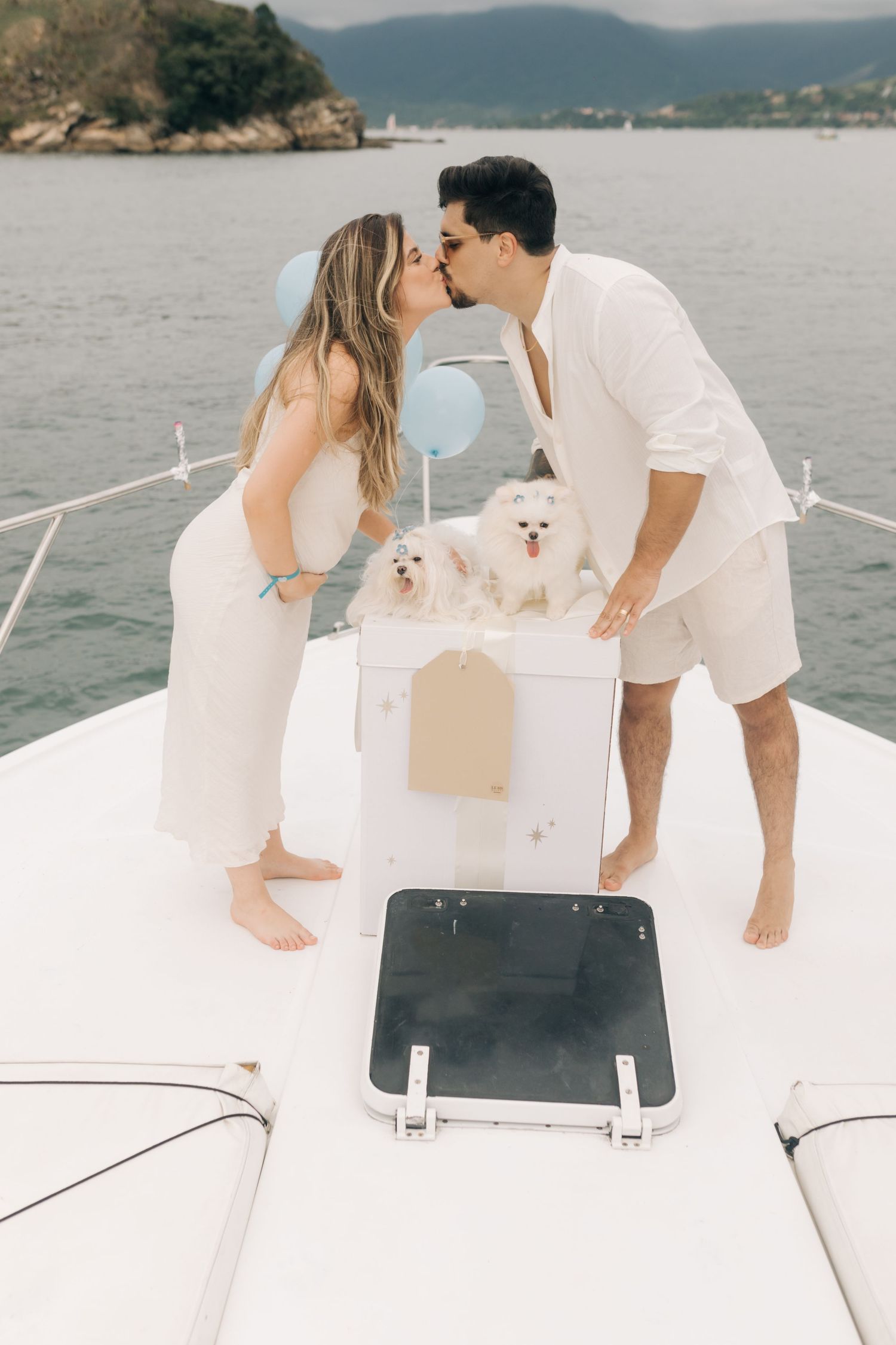 Couple sharing moment on boat deck with two small white dogs emerging from decorative box.