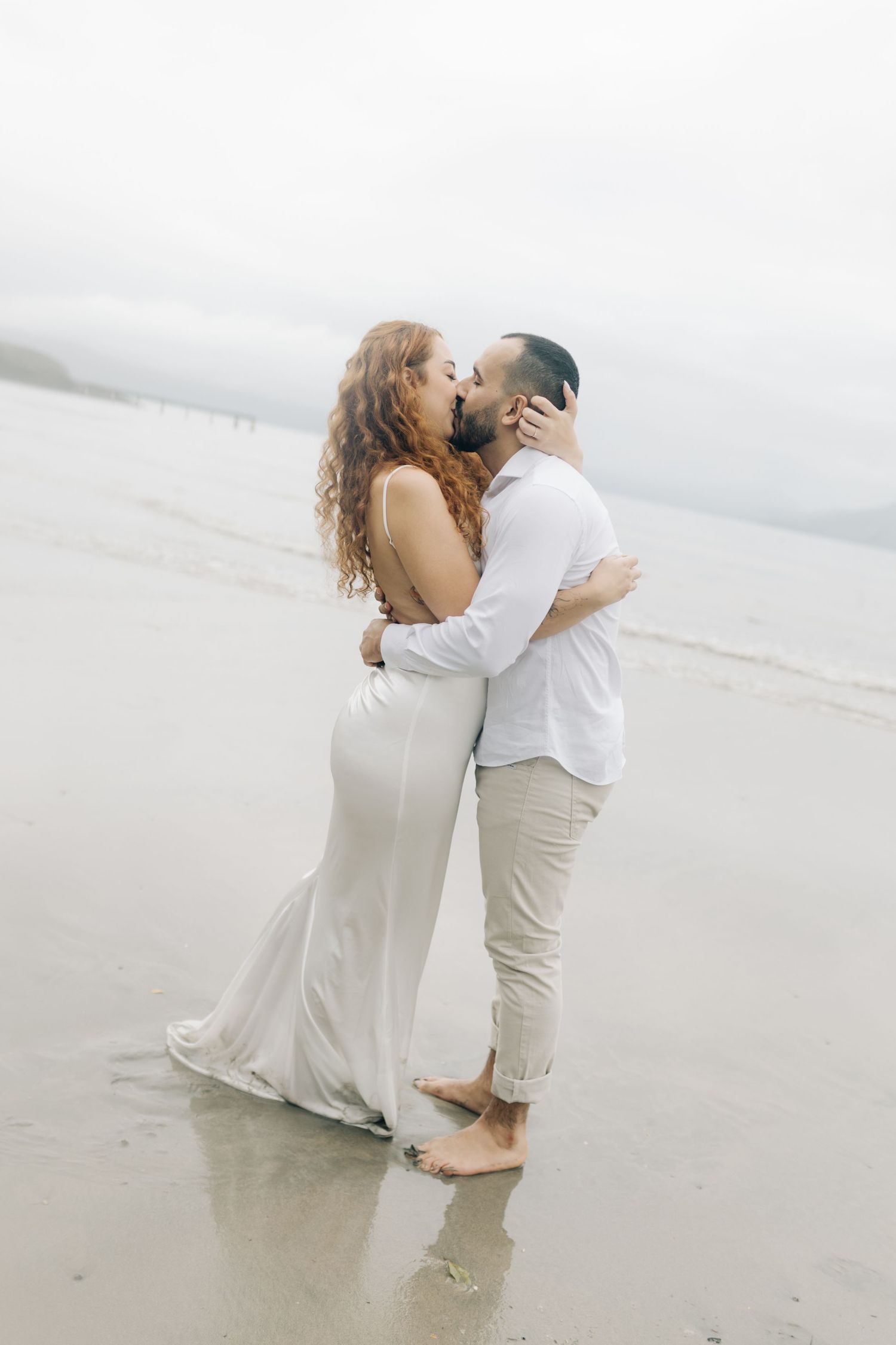 Couple embraces on misty beach shoreline during romantic moment.