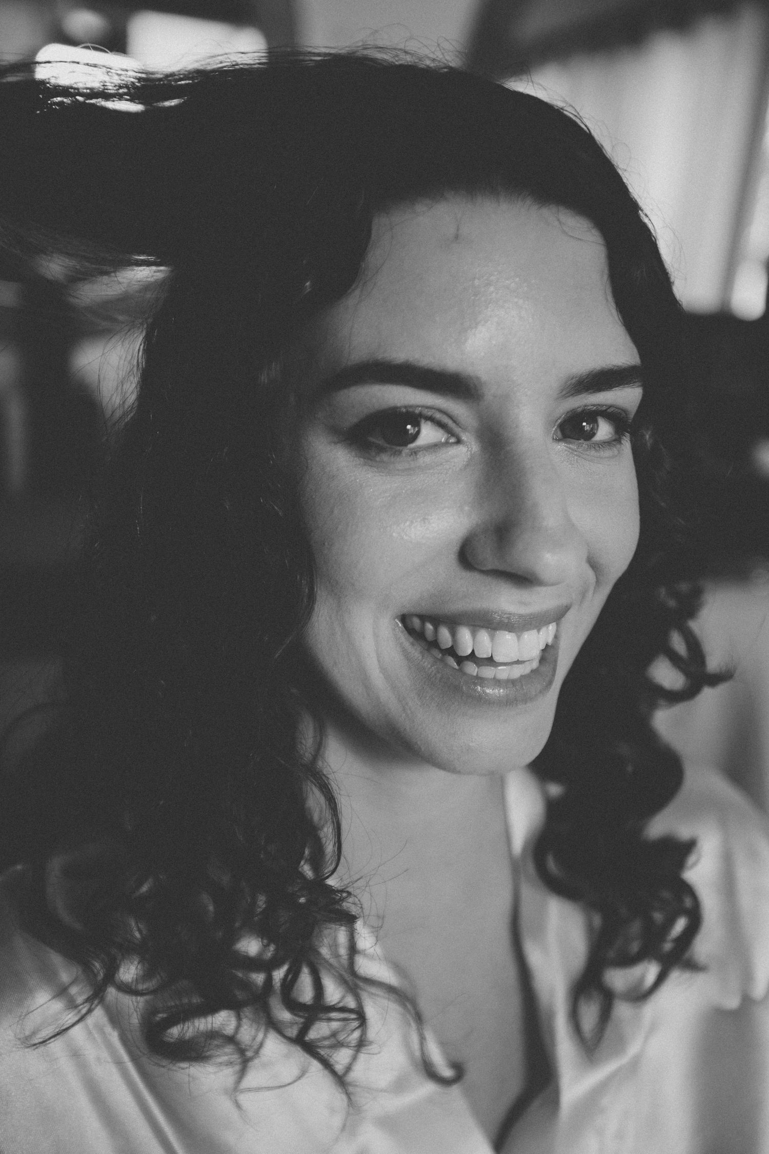 Black and white portrait of someone with dark curly hair and a bright smile.