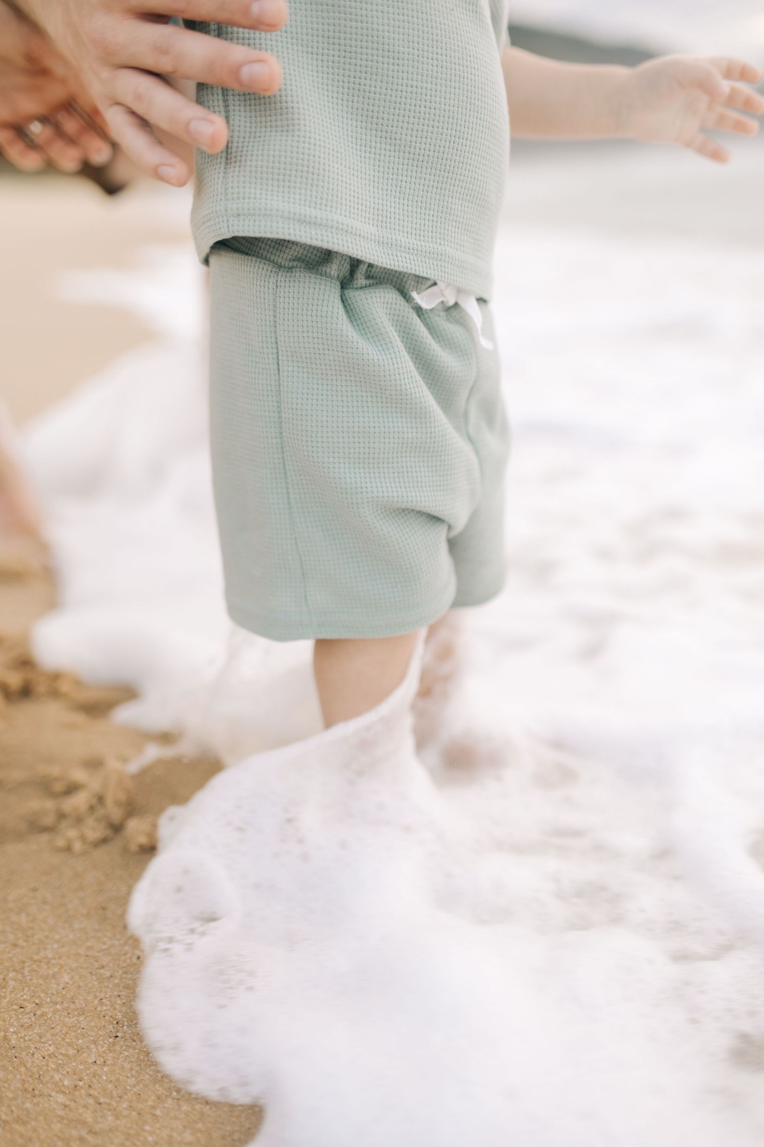 Close-up shot of small feet in the sand as ocean waves roll onto a tropical beach.