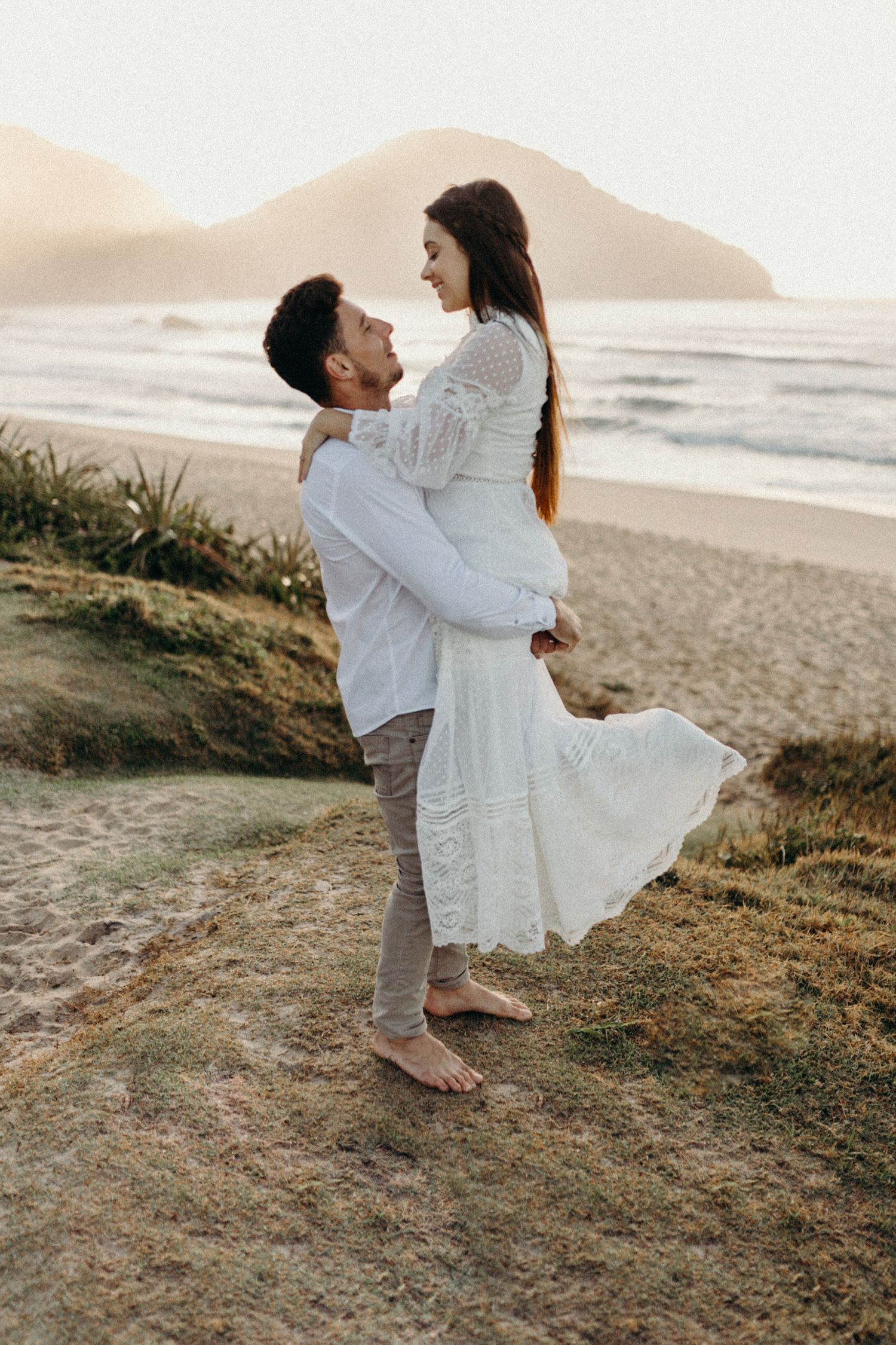 Playful couple twirling on oceanside hill during golden hour.
