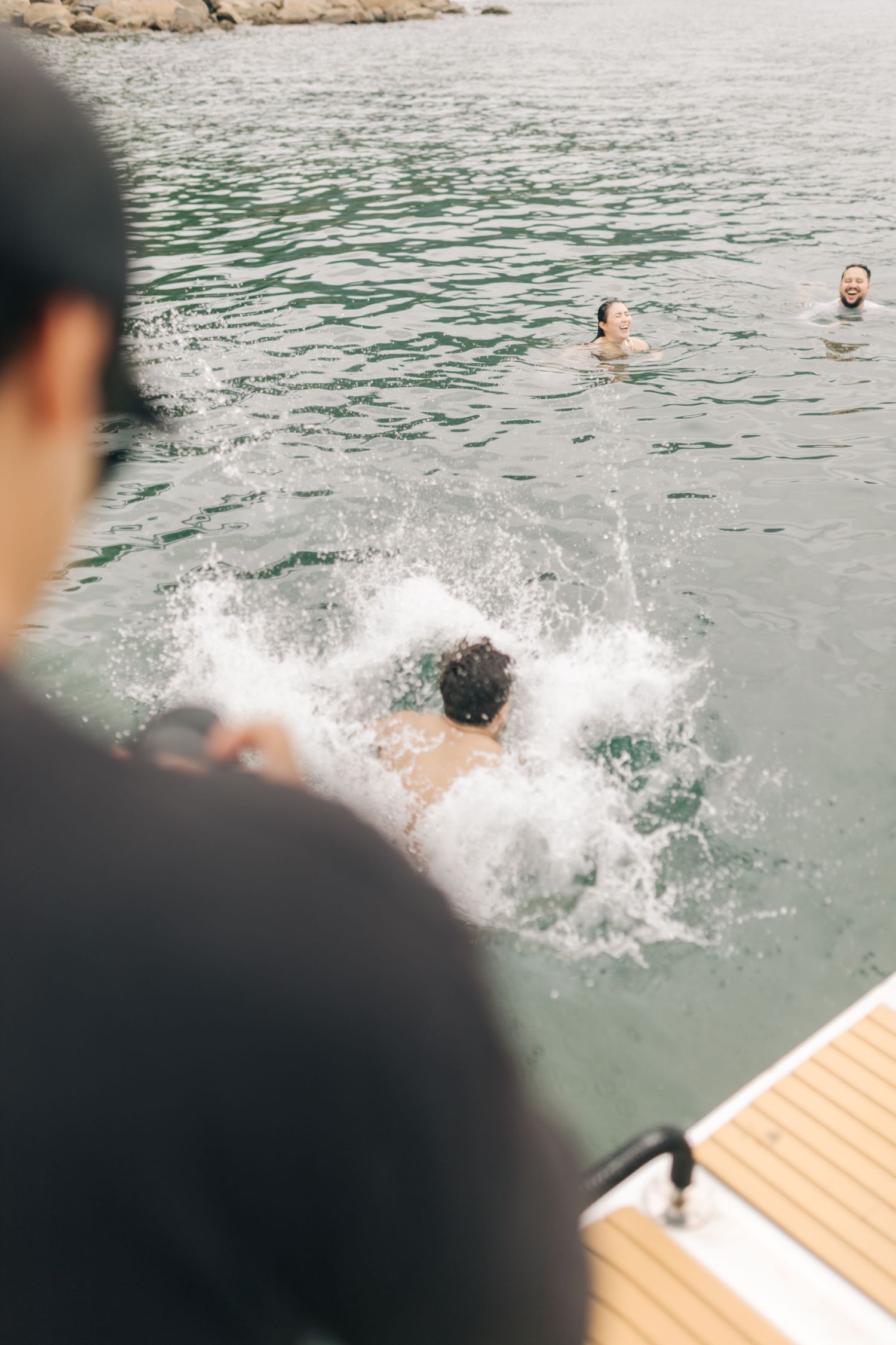 People splashing into water after jumping from boat deck with mountains in background.