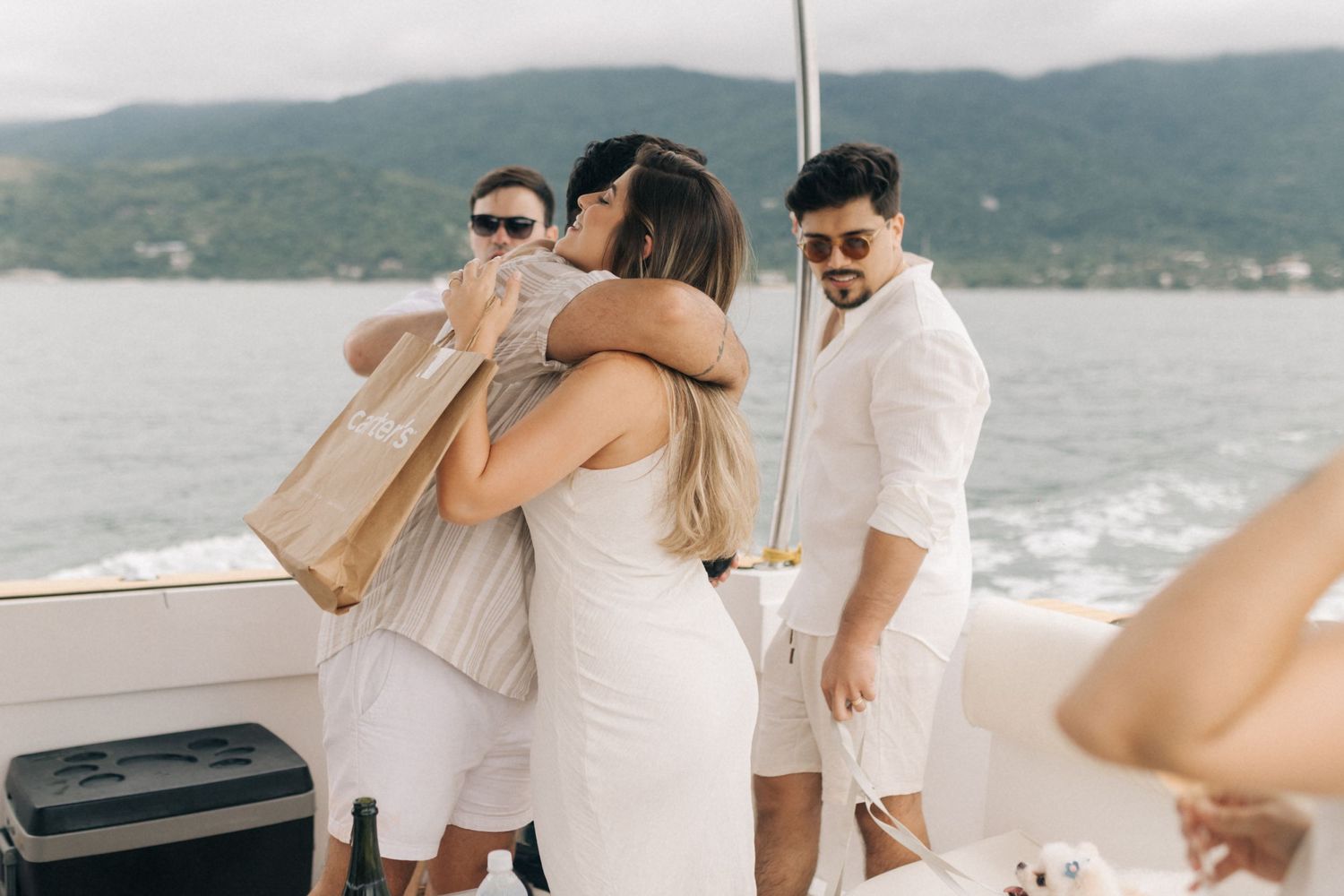 Celebration on boat deck with friends in white outfits sharing emotional moments.