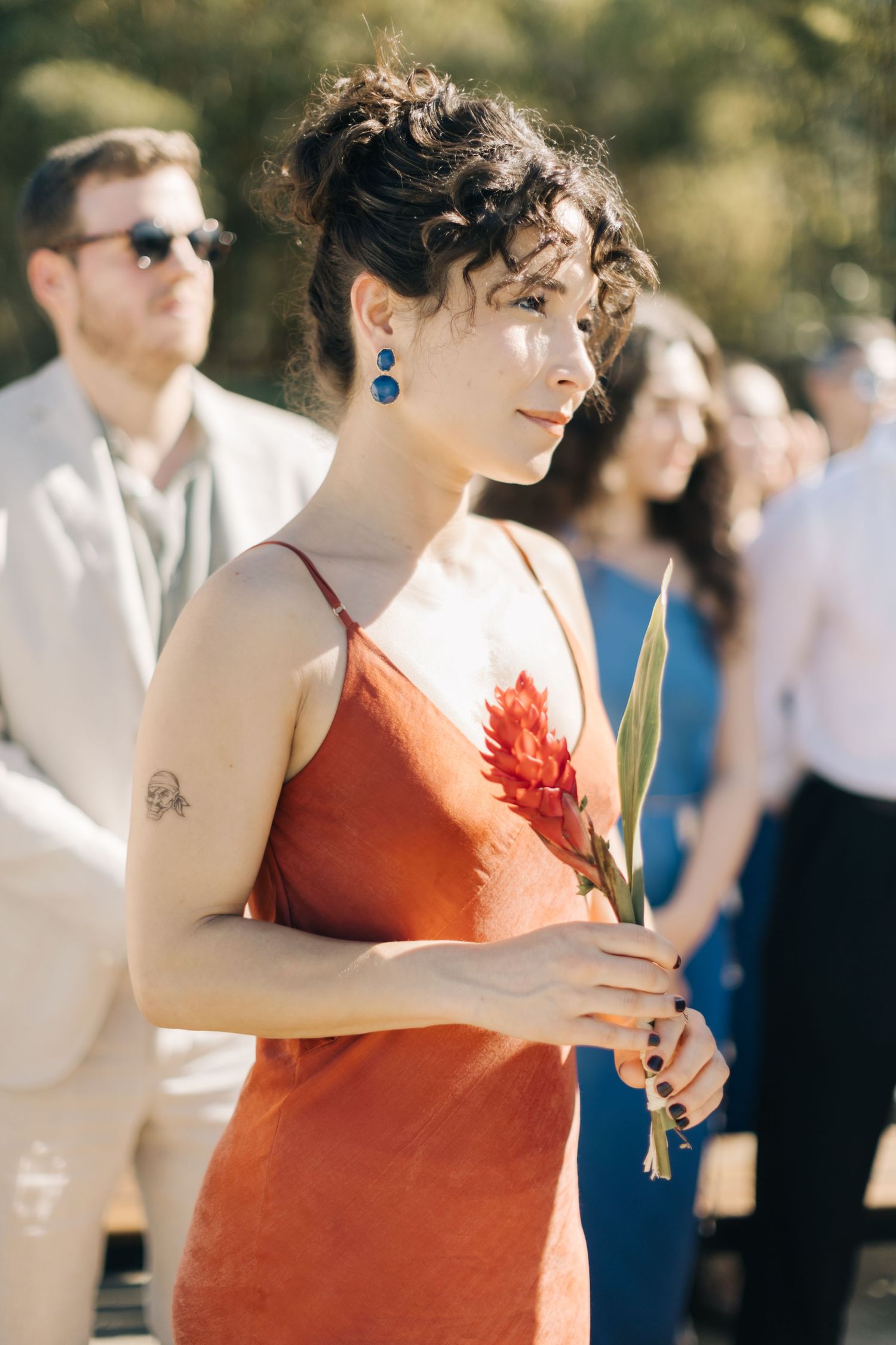 Guest in coral dress with dangling blue earrings at outdoor wedding ceremony.