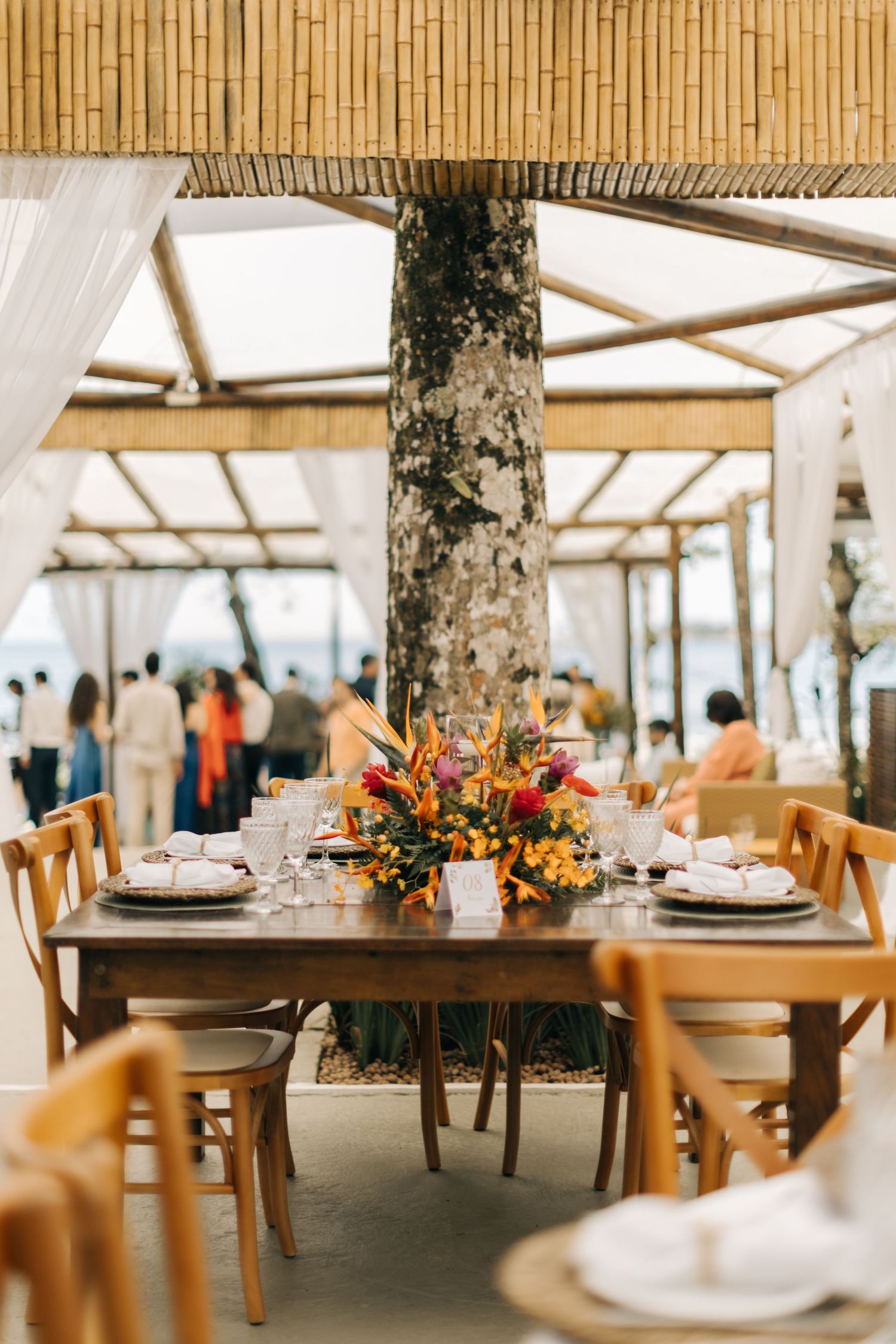 Tropical wedding reception setup with bamboo ceiling and elegant table settings under white draping.