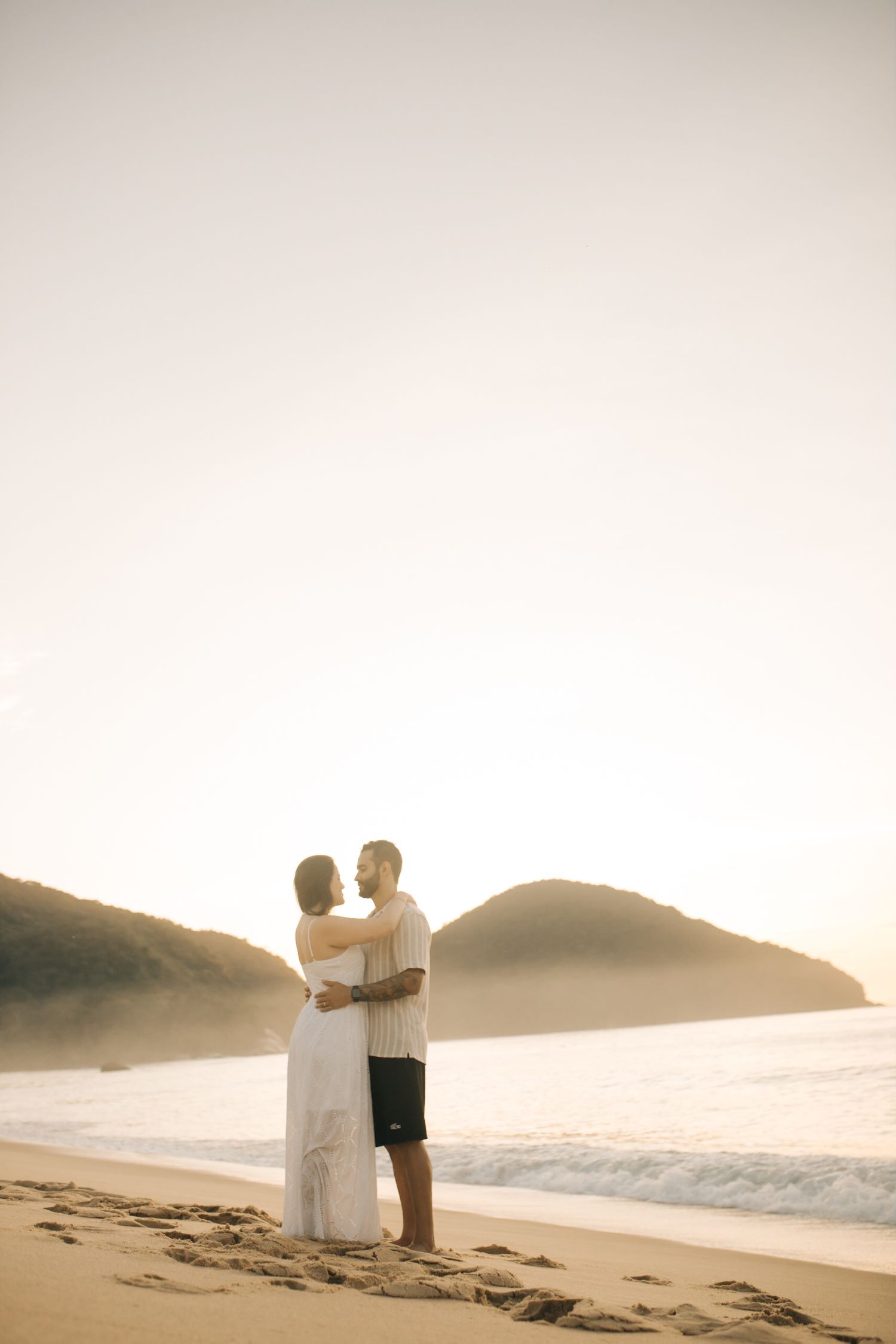 Silhouette of a couple embracing on the beach at sunset with mountains in the background.