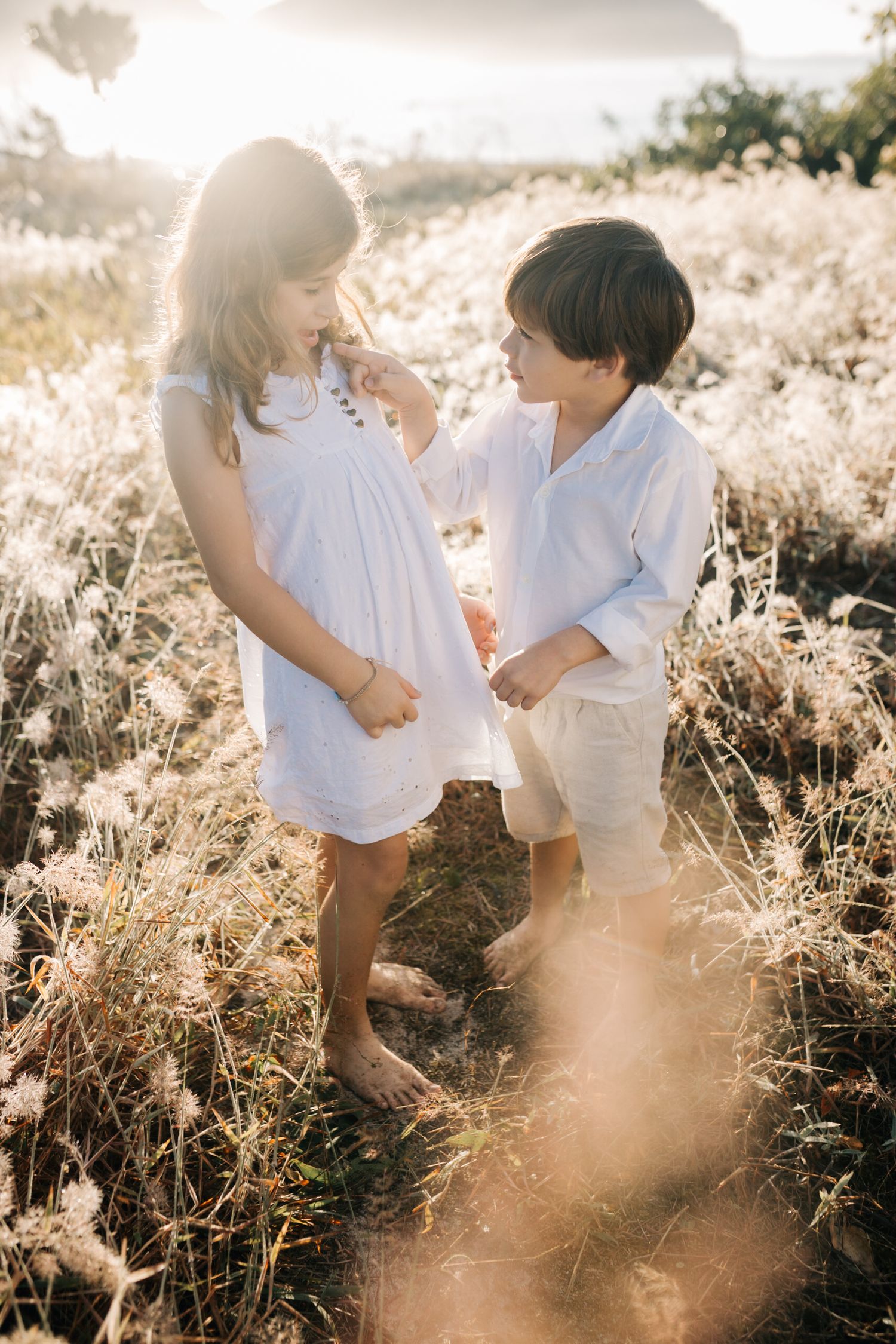 Two small figures in white clothing stand together in sun-drenched golden grass.