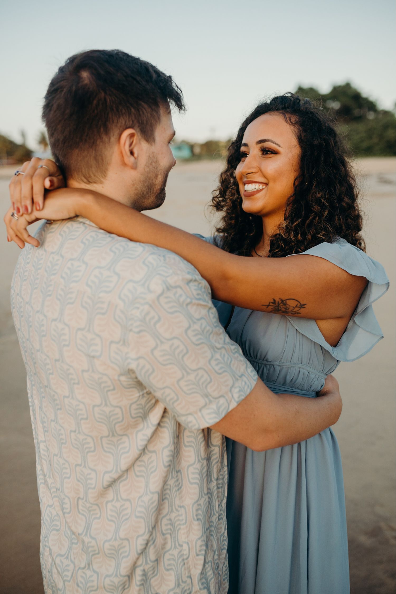 Loving couple embracing on beach during sunset with ocean waves in background.