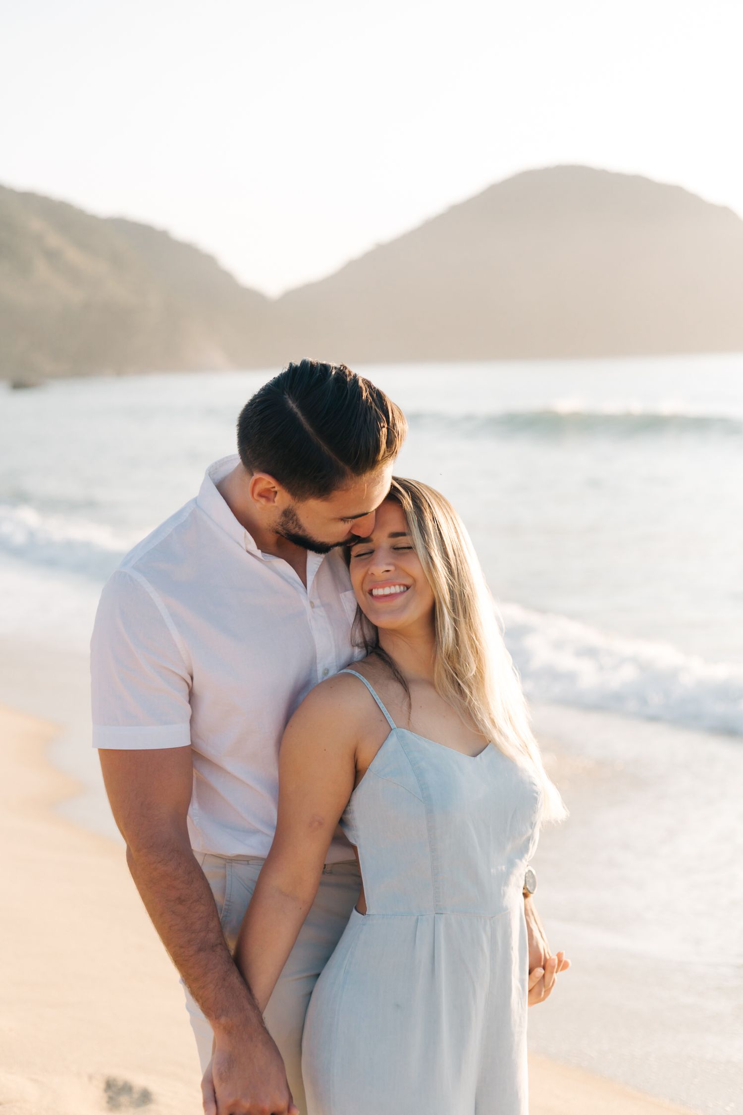 Romantic couple embracing on a beautiful beach at sunset with mountains in the background.
