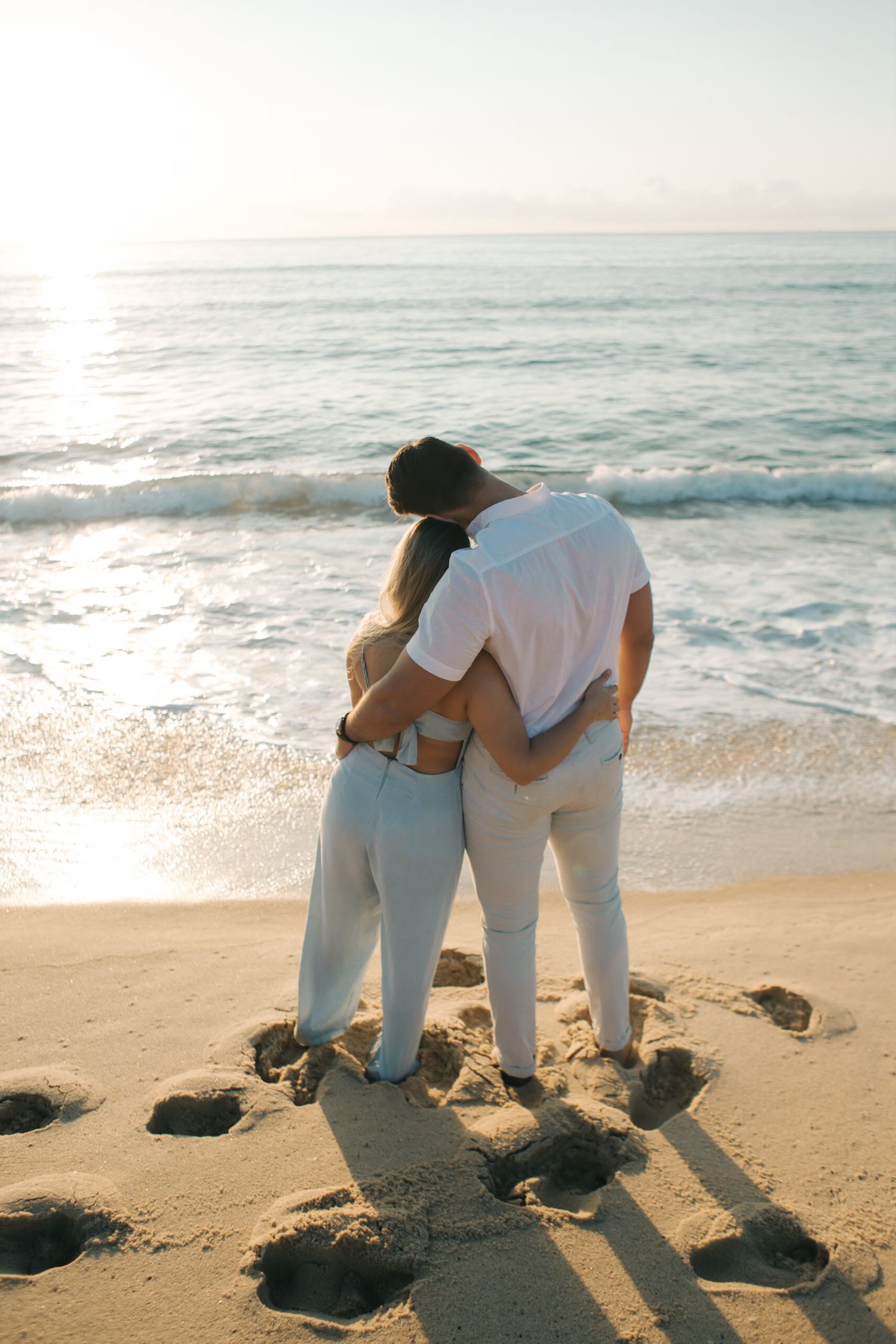 Couple embracing while standing on rocky beach during sunset.