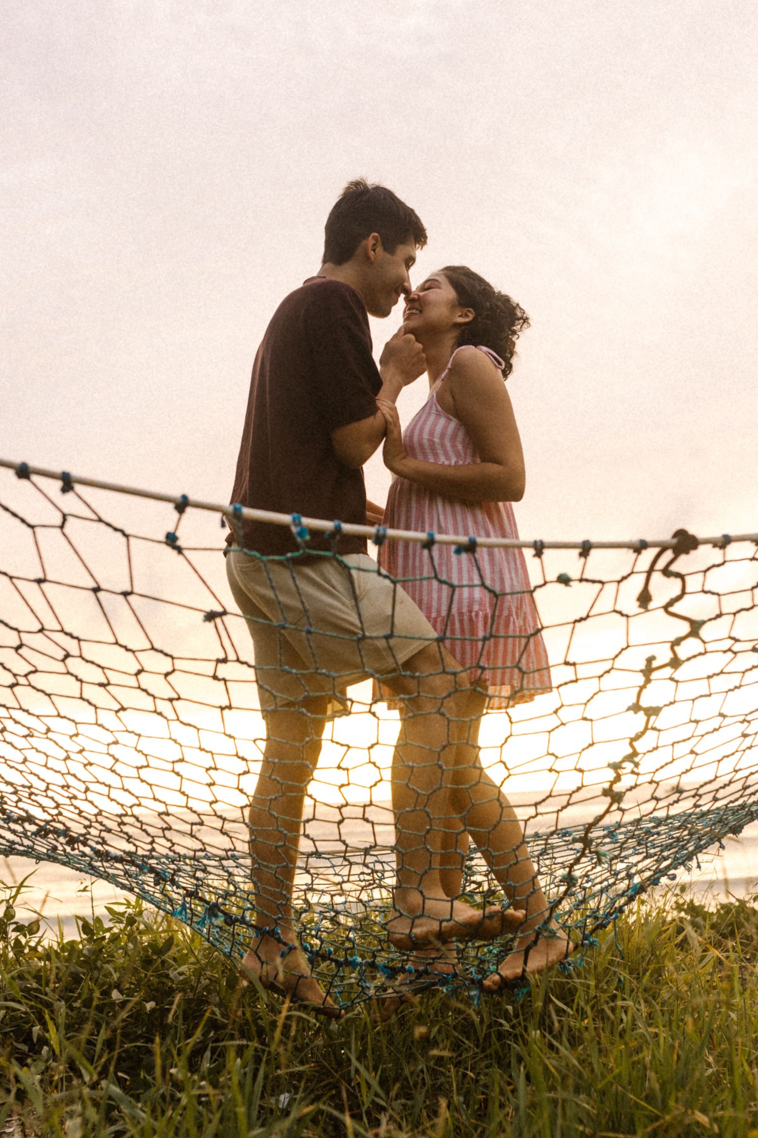 Um casal romântico se abraça em uma rede ao ar livre ao pôr do sol em um belo cenário natural.