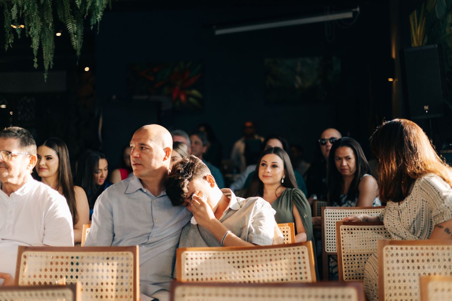 Wedding reception guests seated at tables with warm lighting and cane back chairs.
