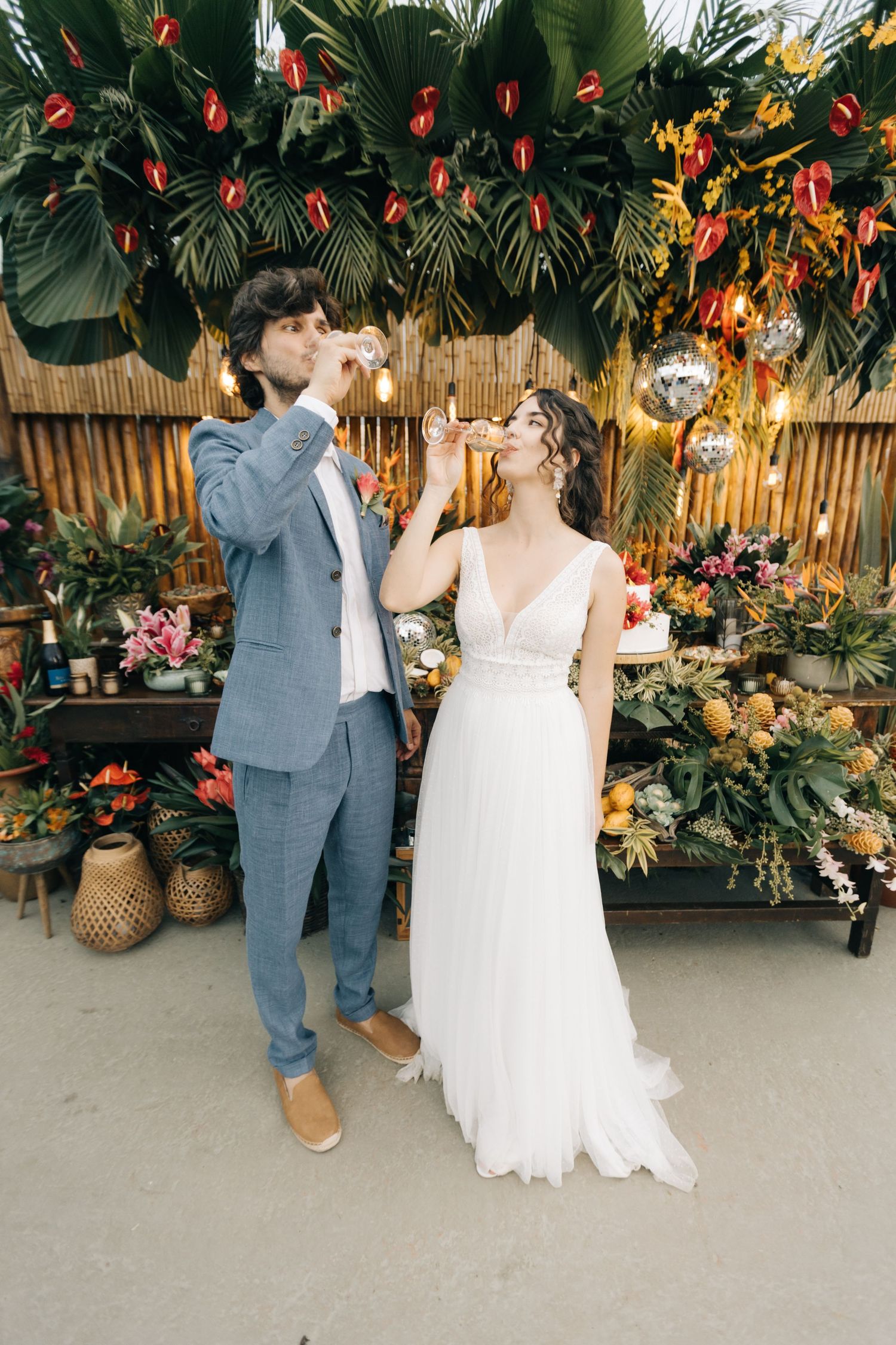 A couple enjoying drinks at their tropical-themed wedding with bamboo and string lights.