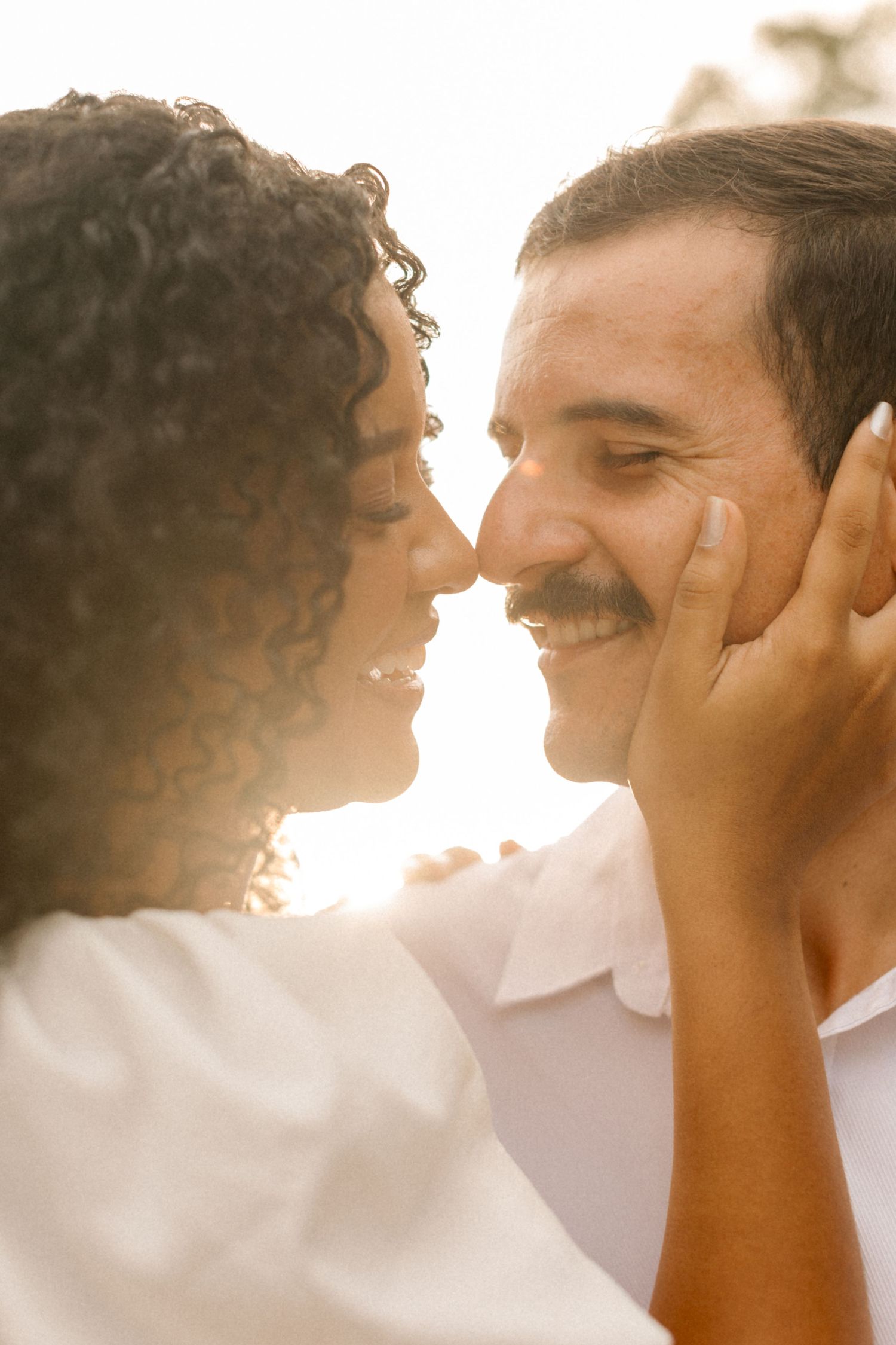 A romantic couple shares an intimate moment in warm golden sunlight as they gaze lovingly at each other.
