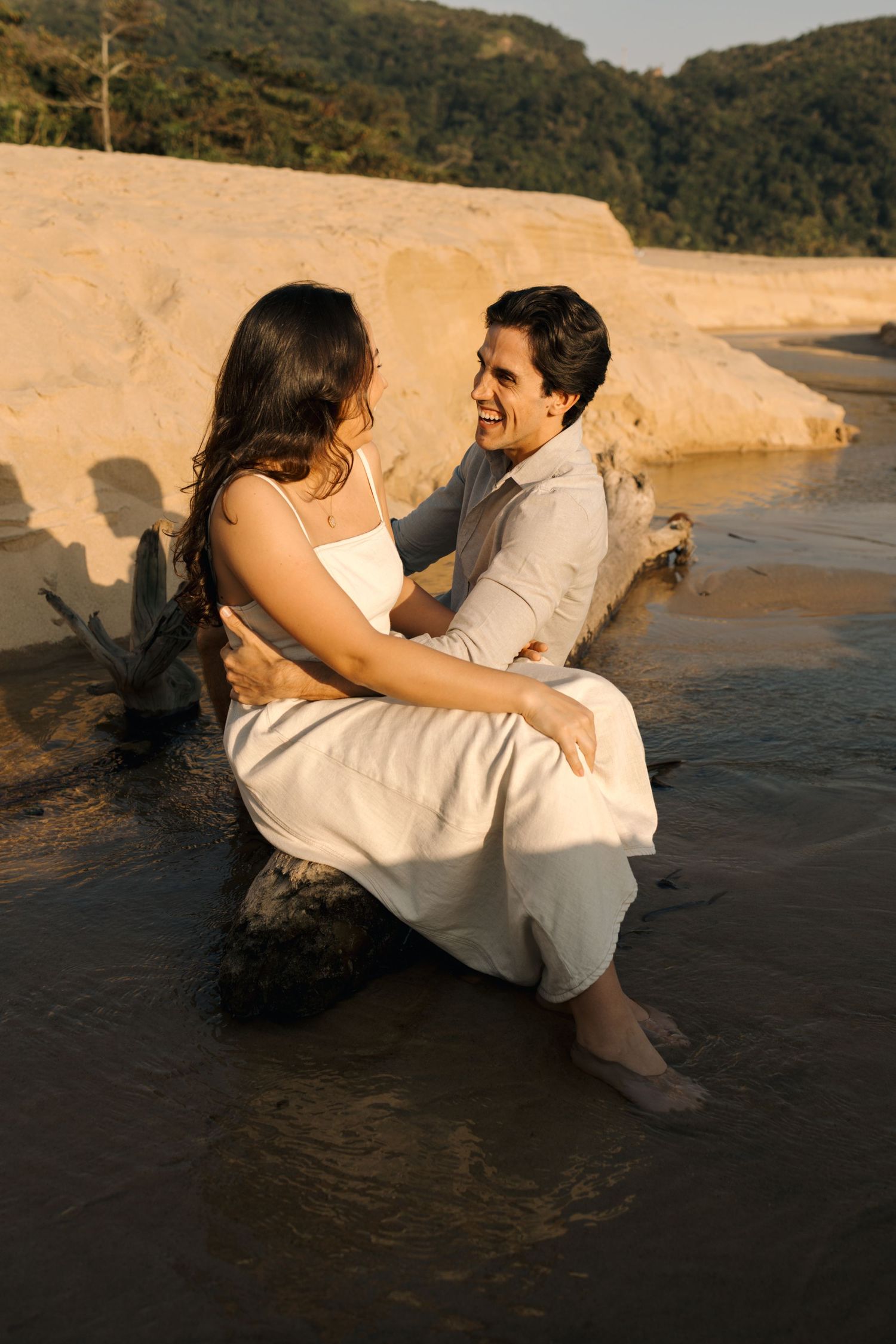 Romantic beach photoshoot with couple playfully posing by the water during golden hour.