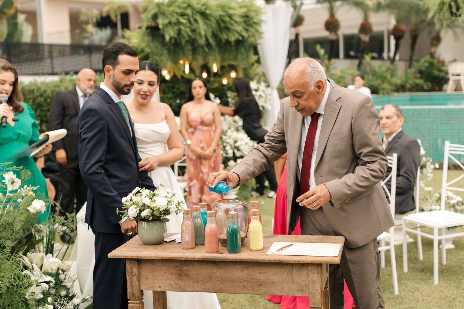 Outdoor wedding ceremony showing guests participating in a special ritual at a wooden table.
