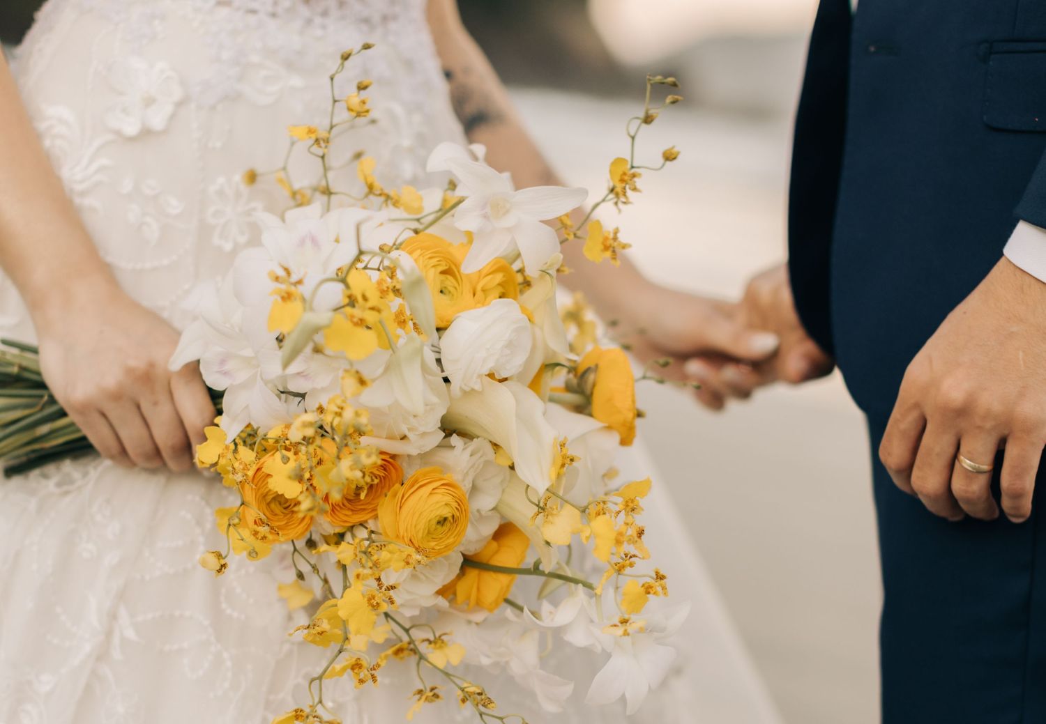 Close up of a bridal bouquet featuring yellow and white flowers with delicate stems against a wedding dress.