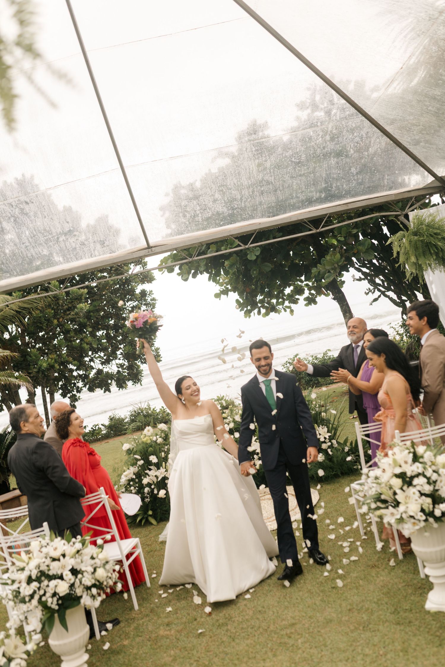 Wedding celebration under a tent with guests throwing confetti as newlyweds celebrate.