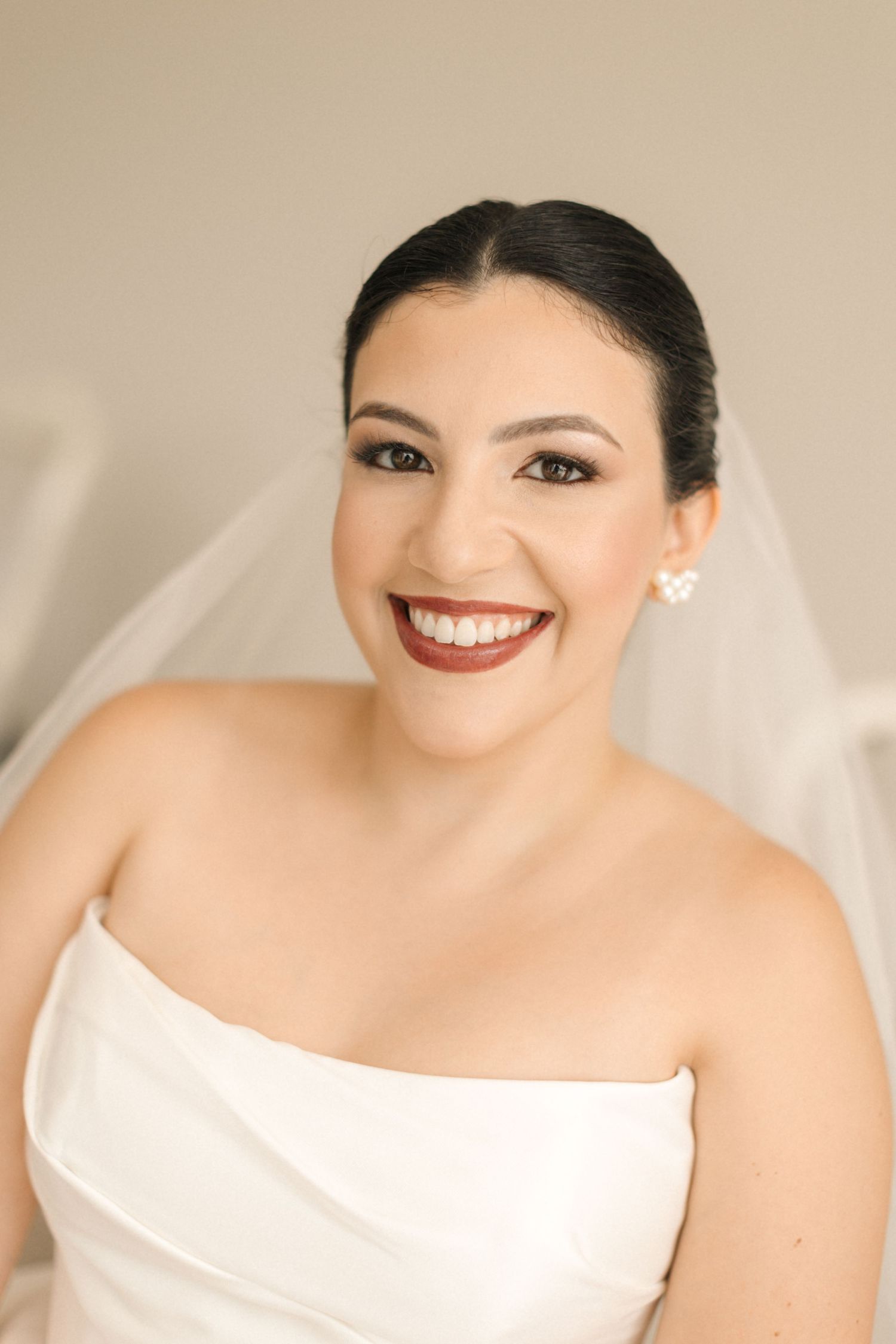 Elegant bride wearing strapless white dress and veil with pearl earrings.