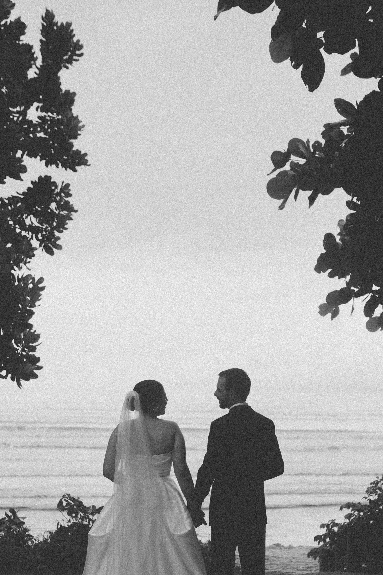 Black and white silhouette of newlyweds overlooking the ocean at sunset.