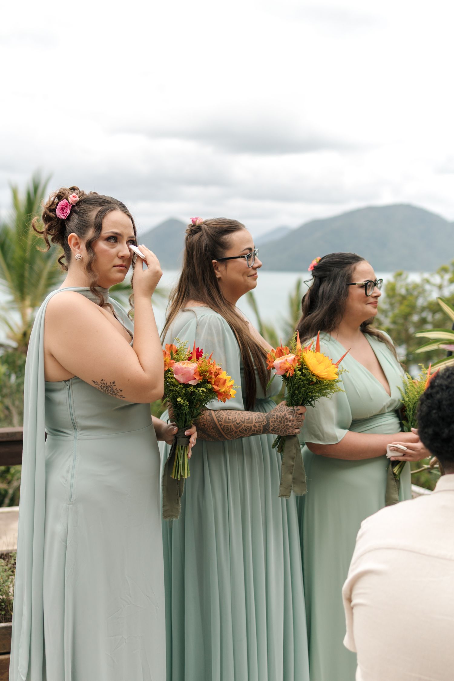 Bridesmaids in sage green dresses hold colorful bouquets while posing with mountains in the background.