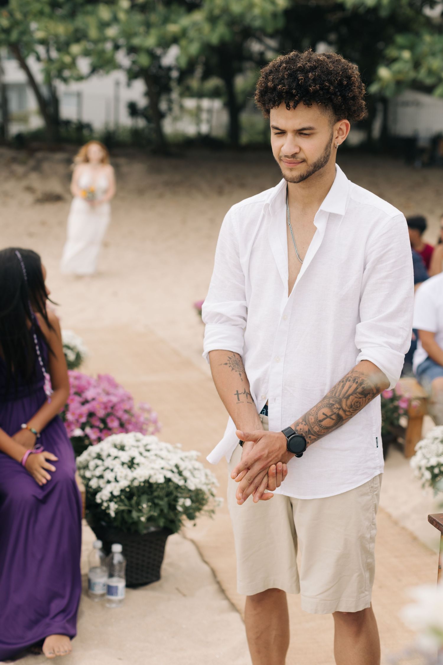 Casual beach wedding gathering with white and purple attire and floral decorations.