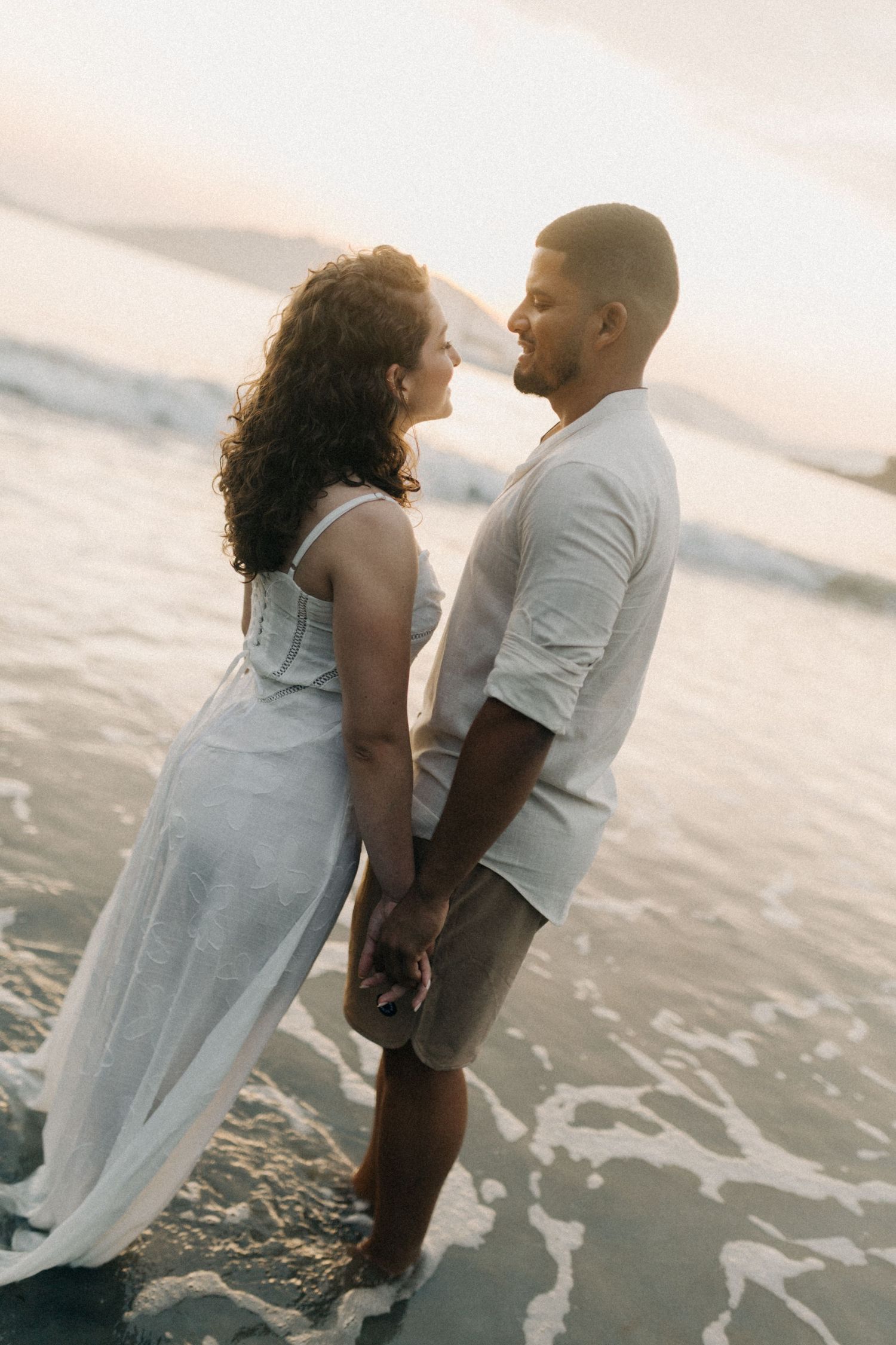 Couple sharing tender moment on beach with ocean waves behind them.