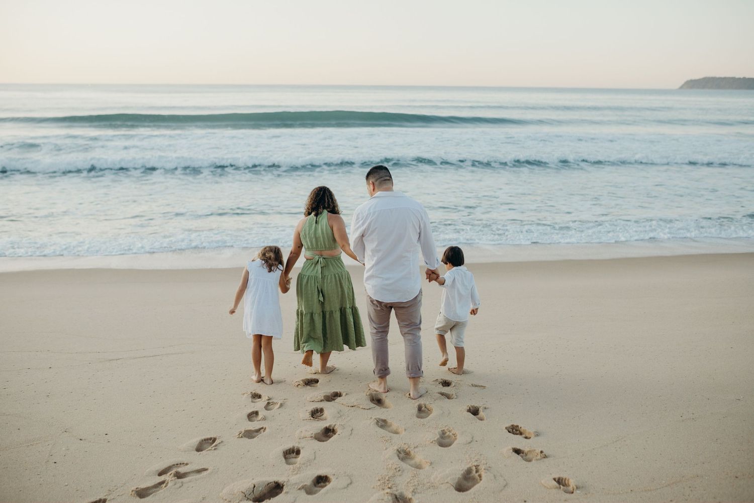 Family walking together leaving footprints on sandy beach at sunset.
