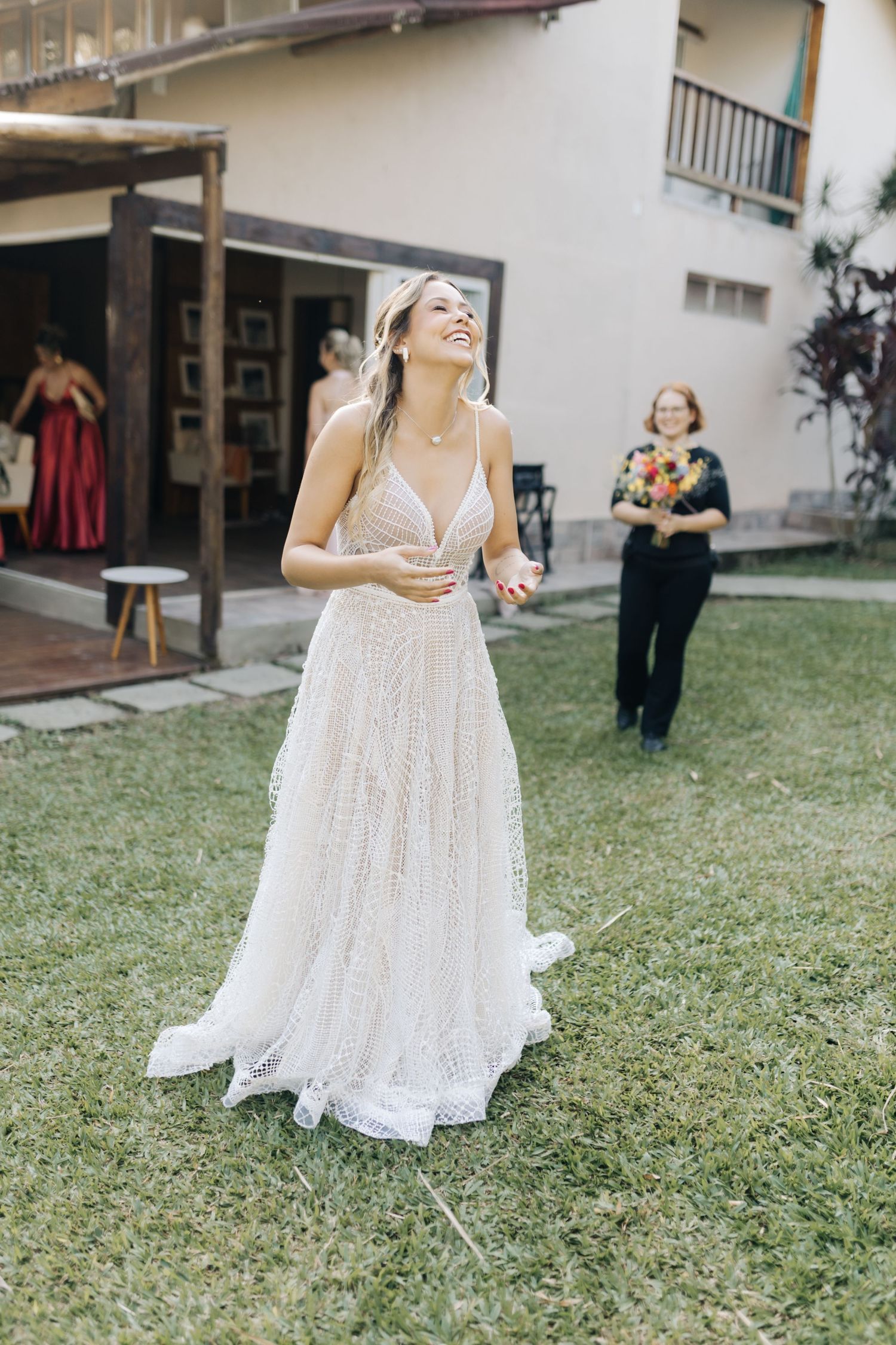 An elegant figure laughs joyfully while wearing a white lace wedding gown outdoors.
