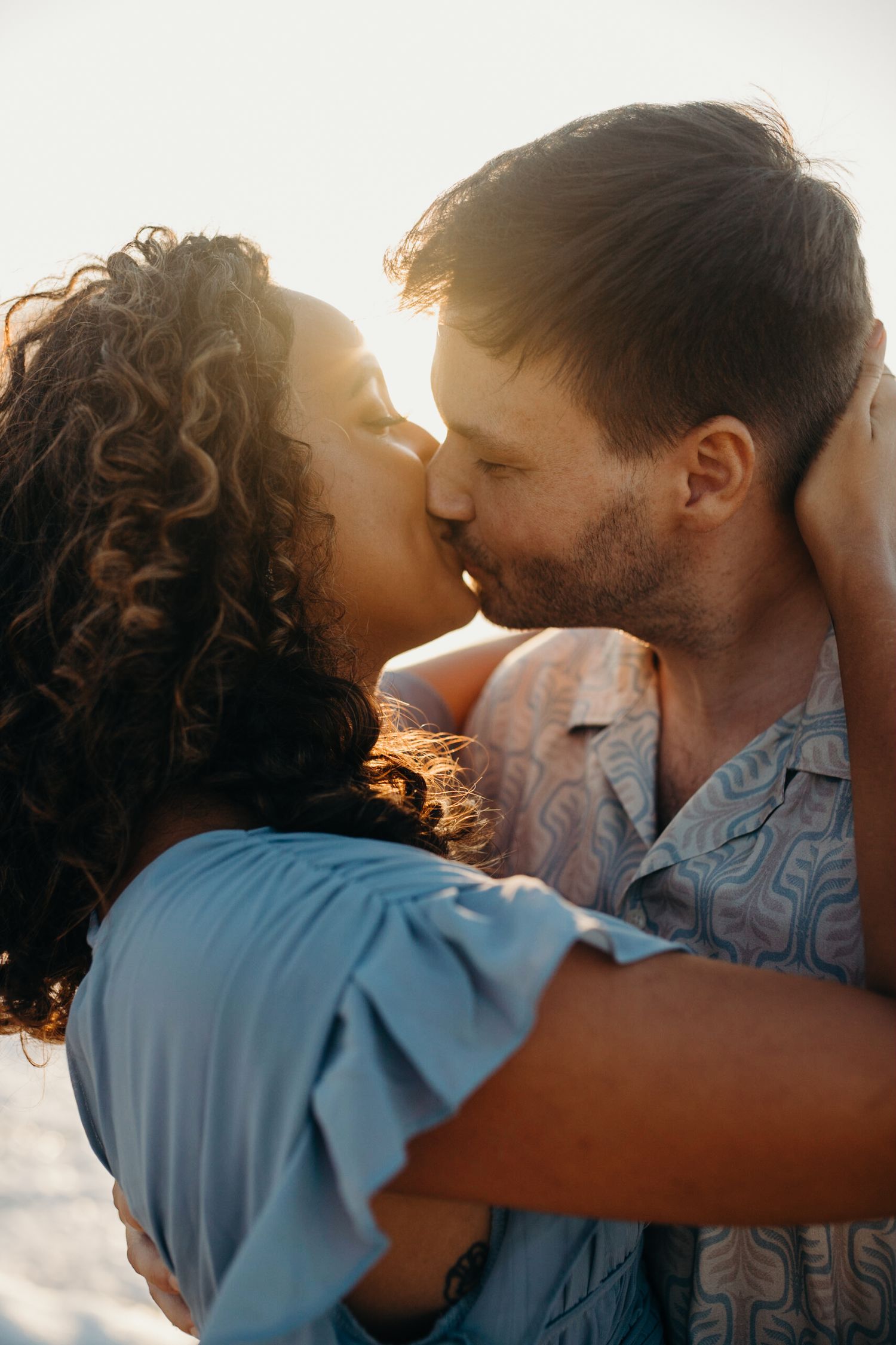 Close-up of couple kissing during sunset beach photoshoot.