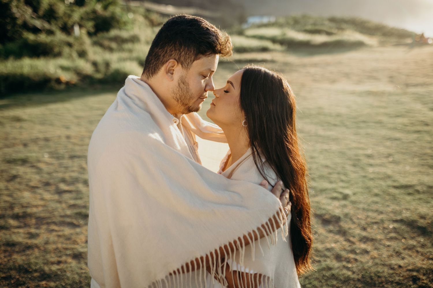 Intimate romantic moment captured in warm sunlight against green natural backdrop.