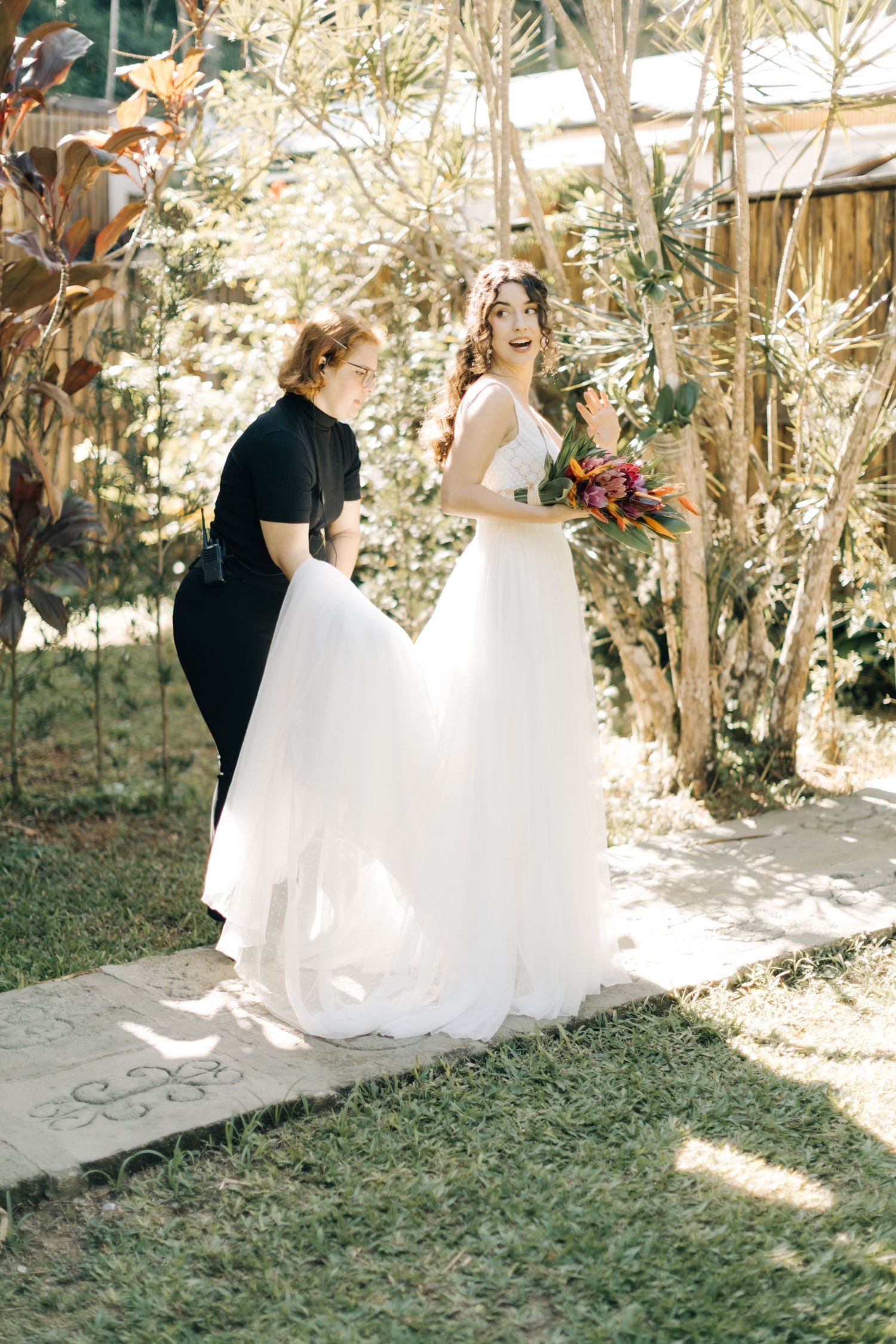 Wedding photography session in a sunlit garden path with flowing white gown.