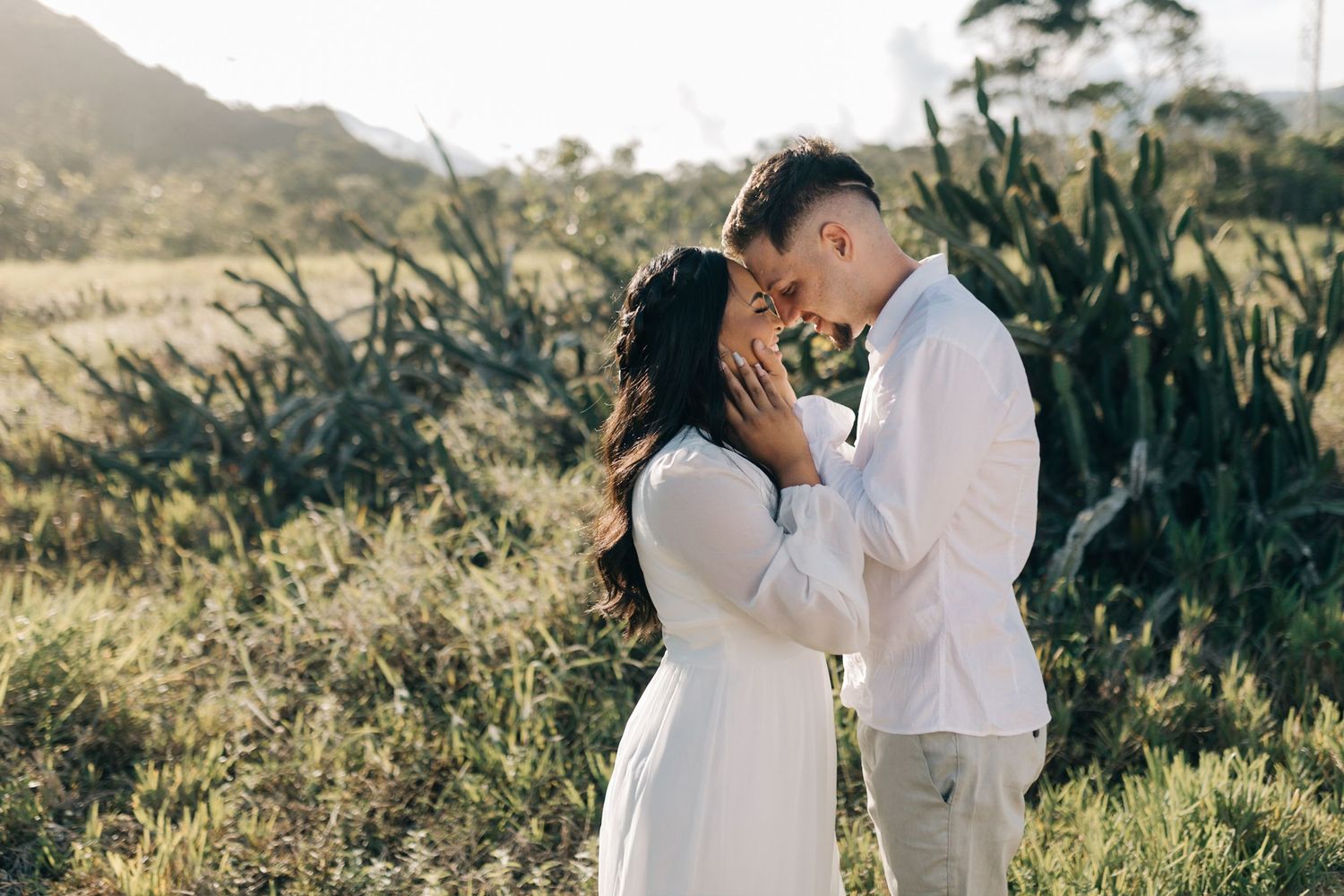 A tender moment between a couple in white attire surrounded by natural scenery.