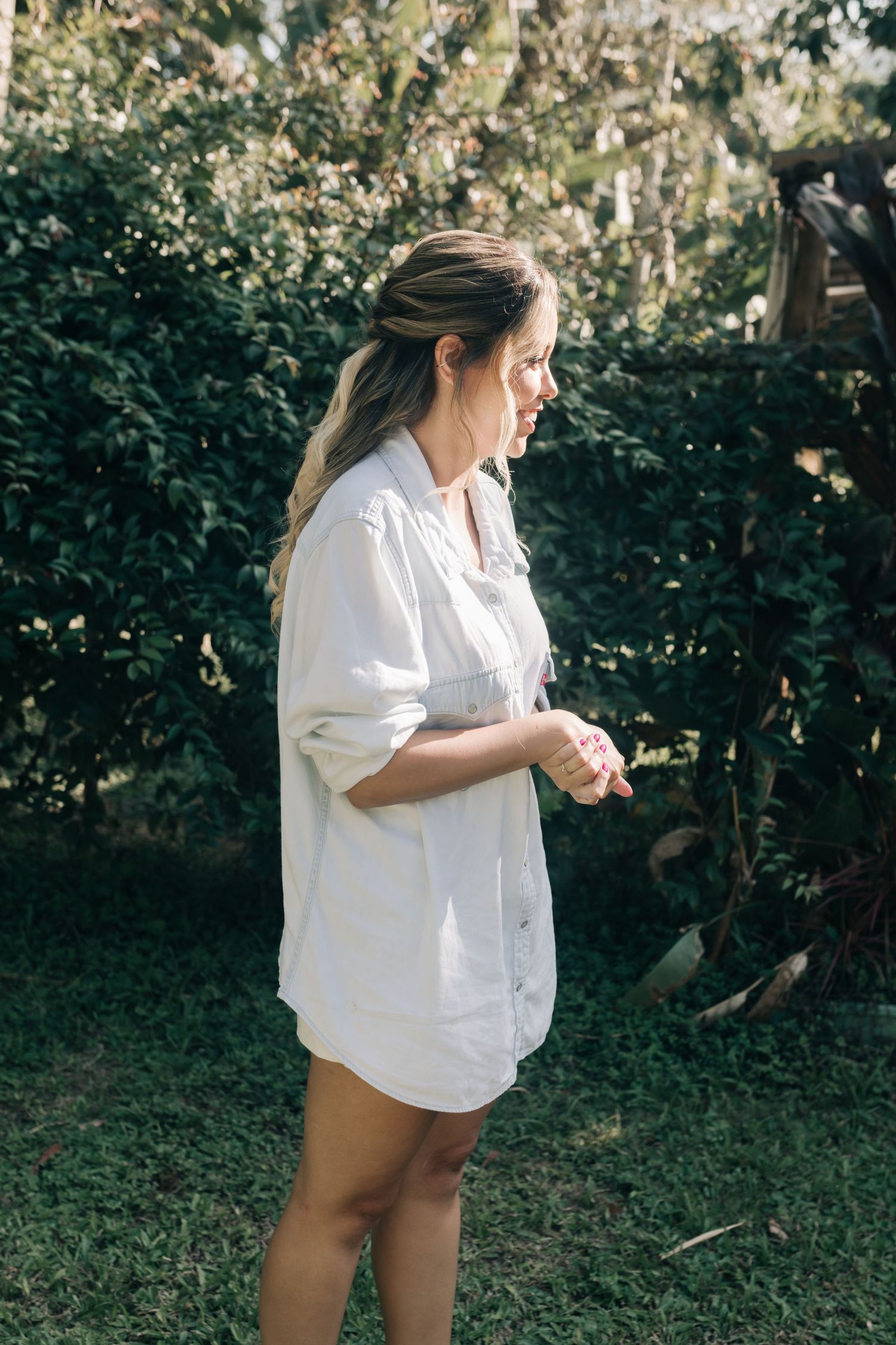 A person in a white button-down shirt stands in profile against a lush garden background.