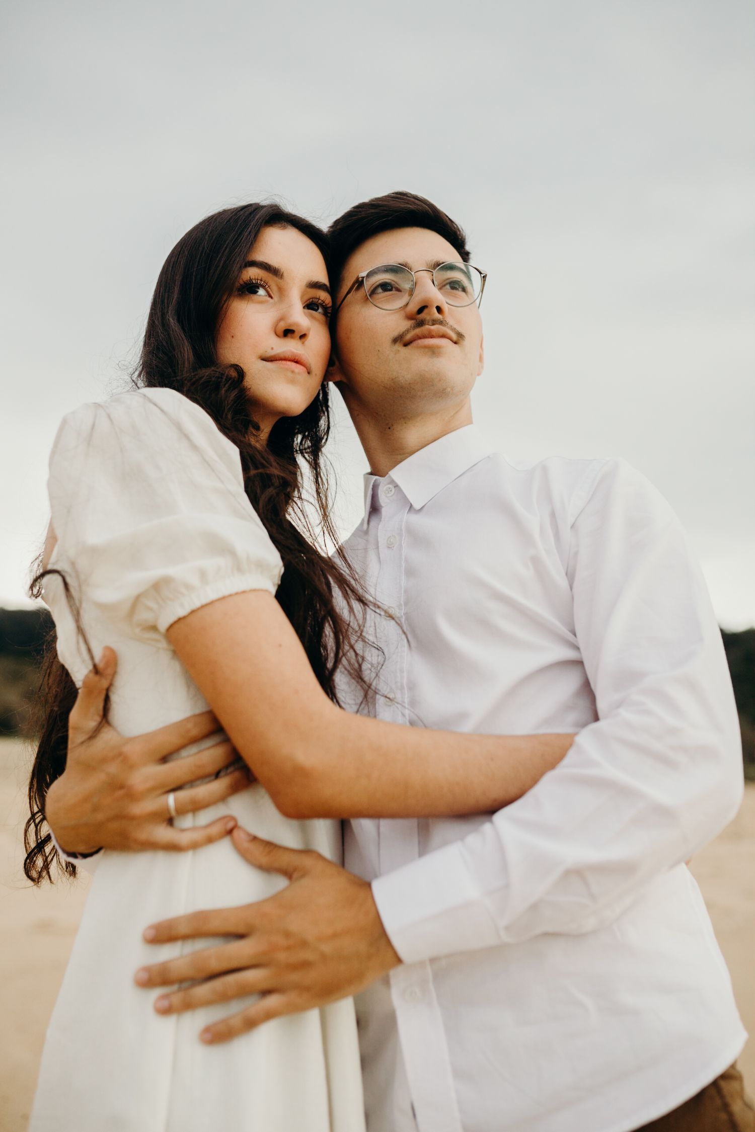 A couple in white embracing against a cloudy sky background.