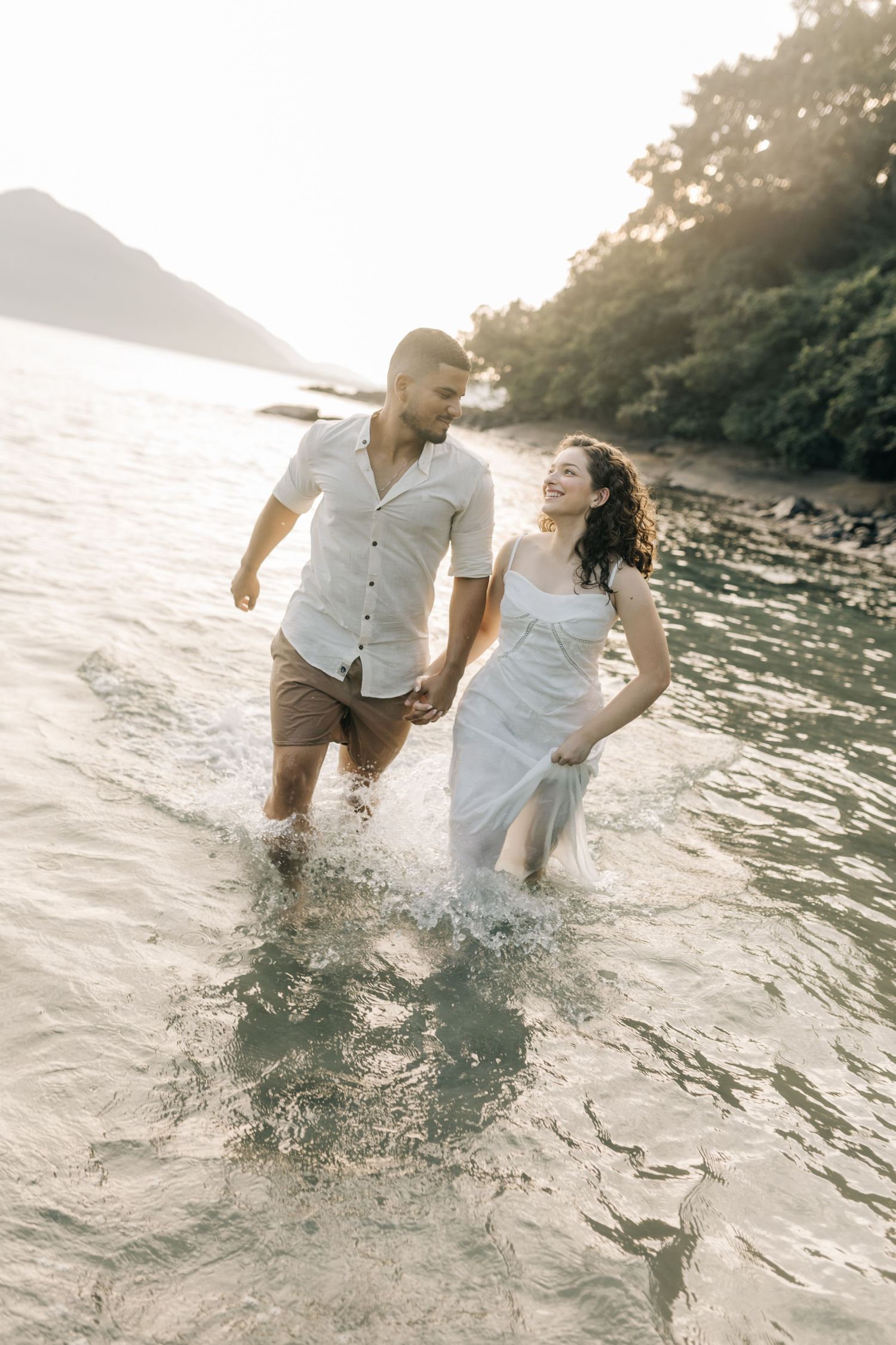 Couple splashing and playing in ocean waves during sunset.