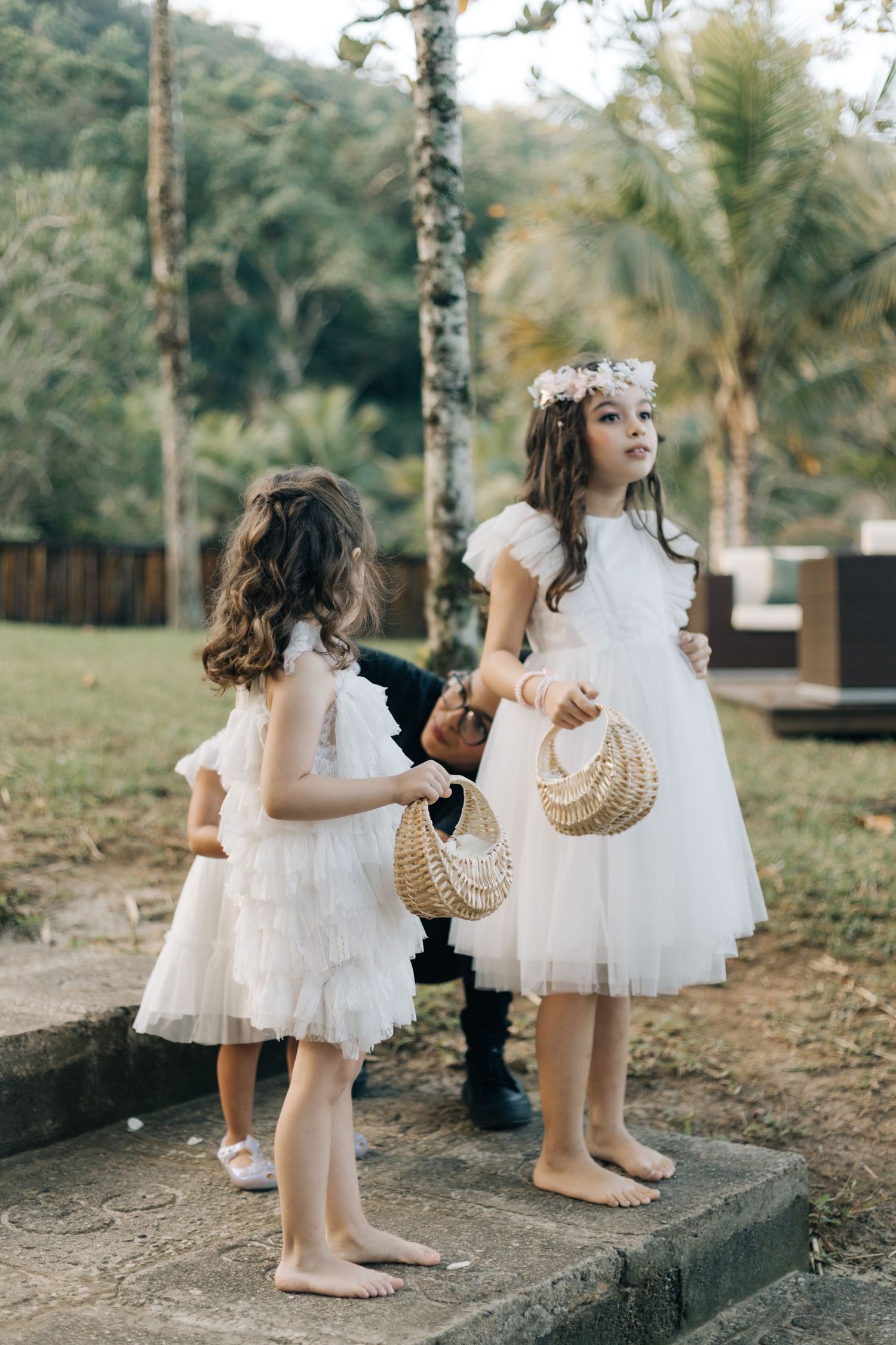 Two attendants in white dresses stand with woven baskets at outdoor celebration.