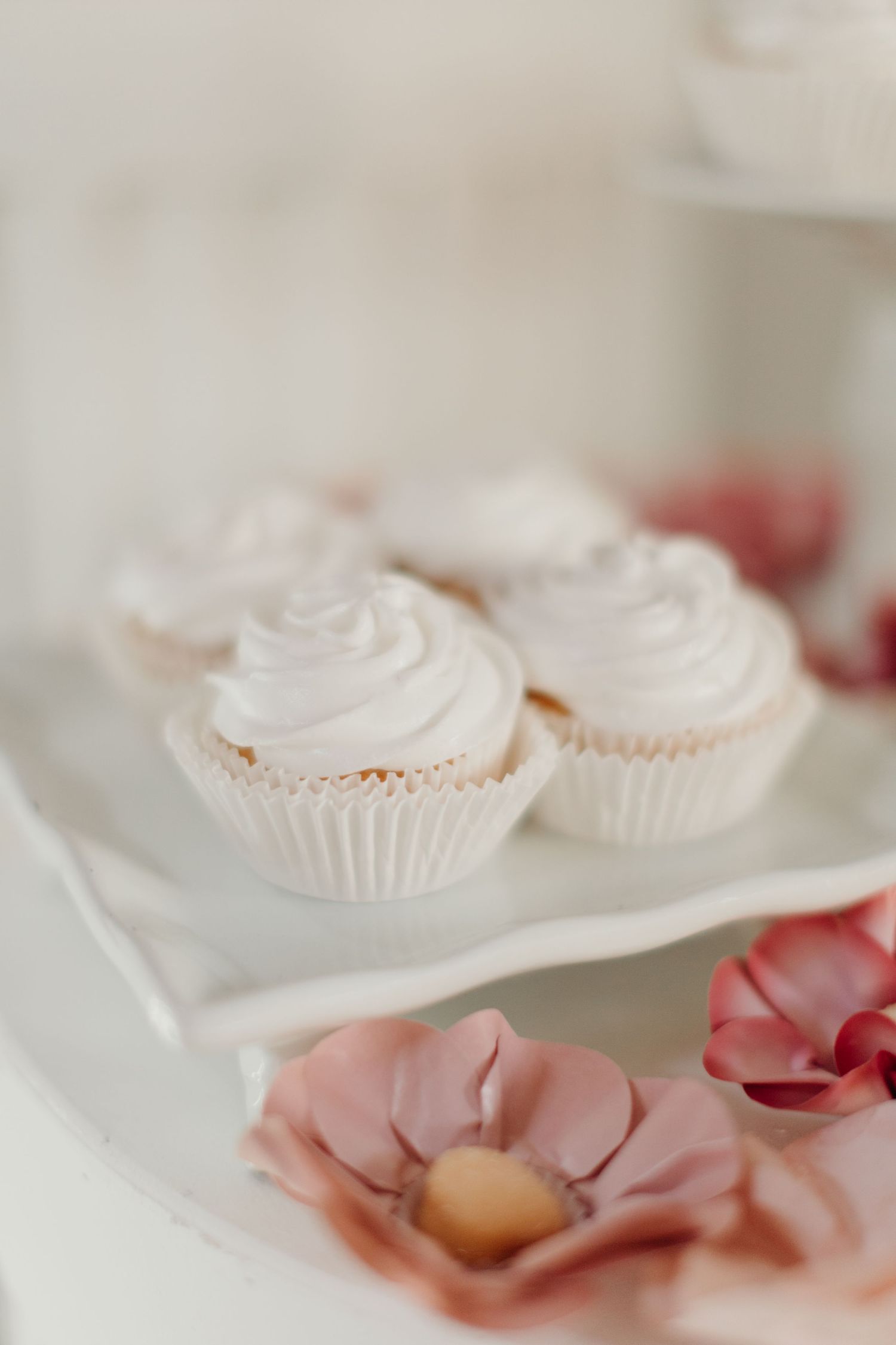 White frosted cupcakes decorated with swirled tops and pink floral accents.