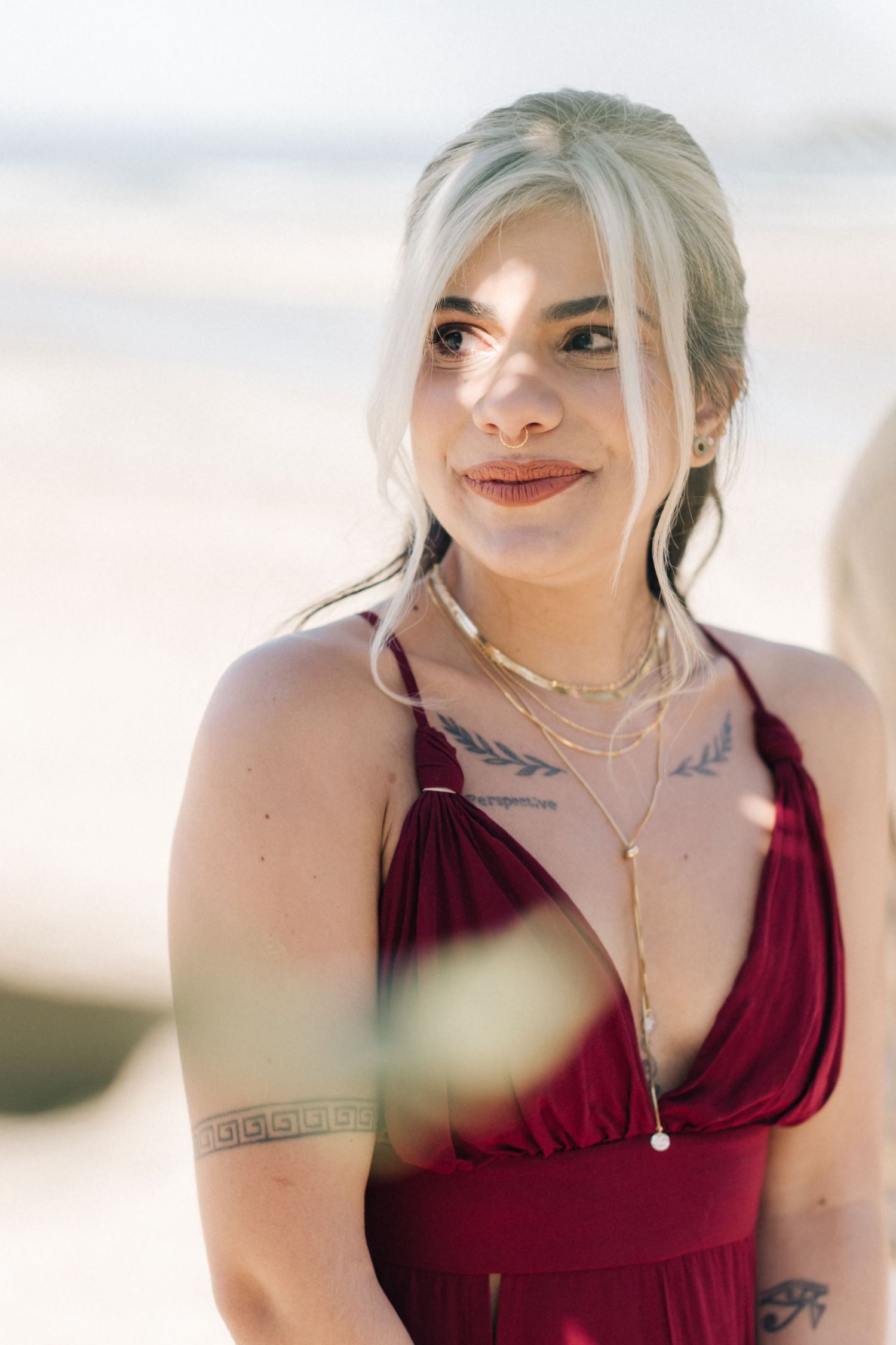 Wedding guest in burgundy dress at beachside ceremony.