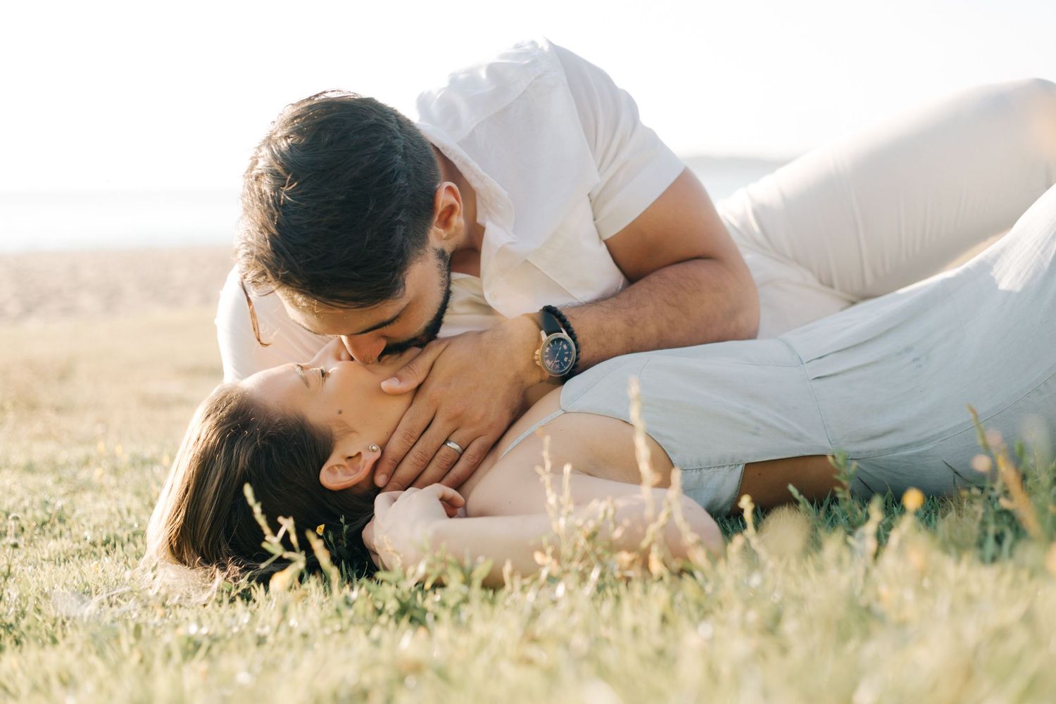 Romantic couple embracing in sunlit meadow during golden hour photoshoot.