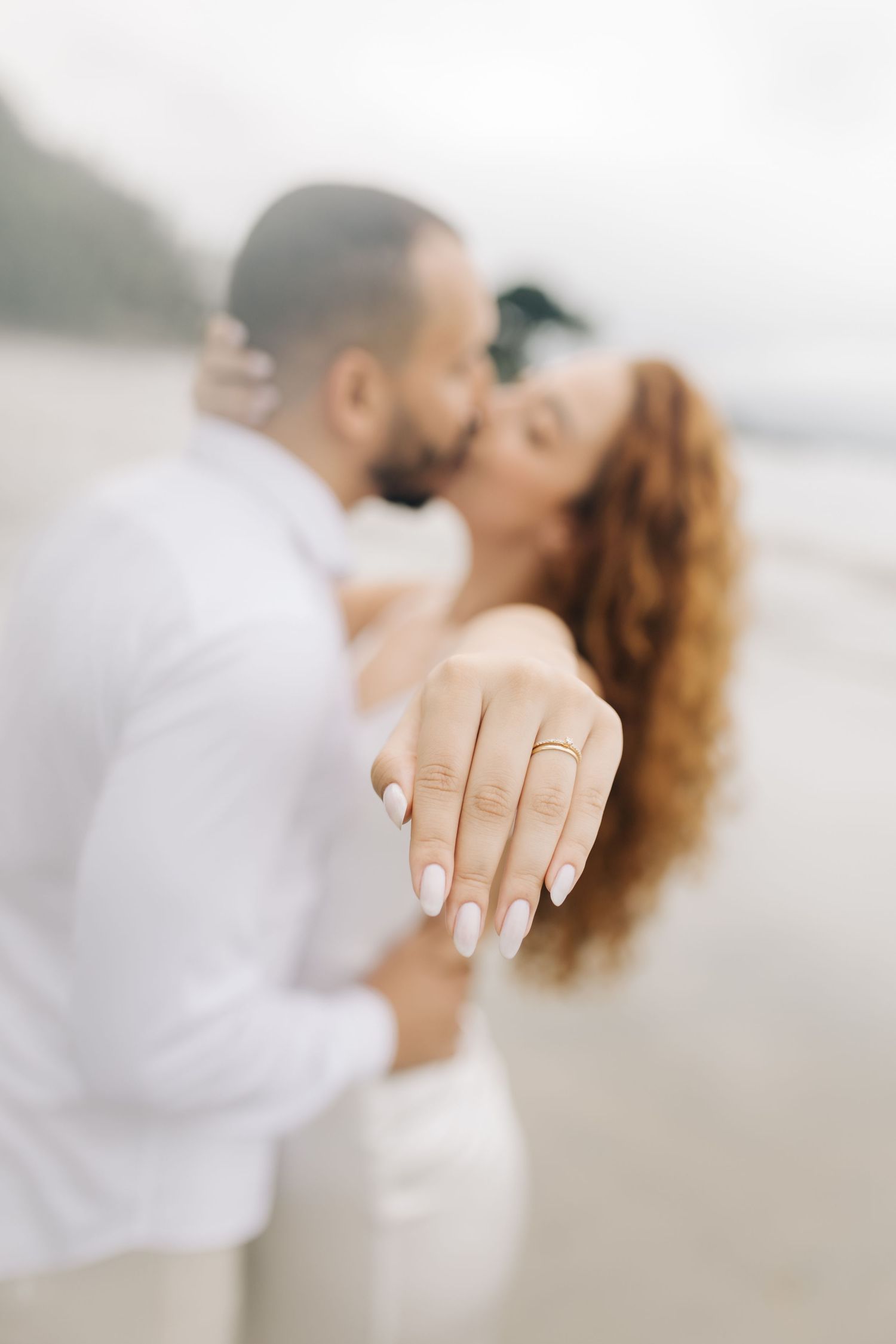 Engagement ring showcase with romantic couple embracing in soft focus background.