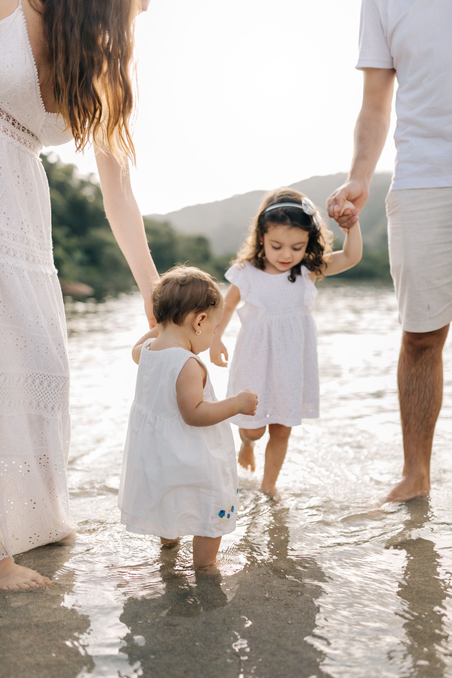 People in white outfits walking together through shallow beach water.